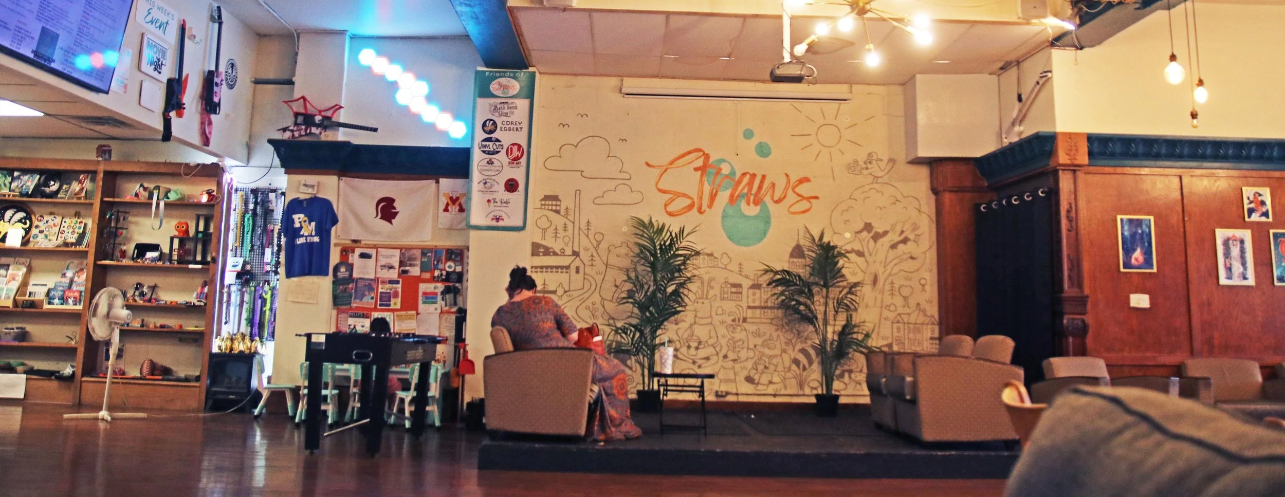 Inside view of Straws soda shop in Buena Vista, Virginia., from left to right, local items for sale, foosball table & bulletin board, stage with plants and armchairs, local art on wall