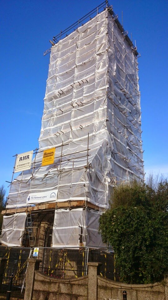 Building under construction covered in white scaffolding and tarps, with clear blue sky in the background.