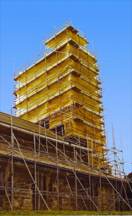 Construction scaffolding around a building with a stone foundation and a blue sky.