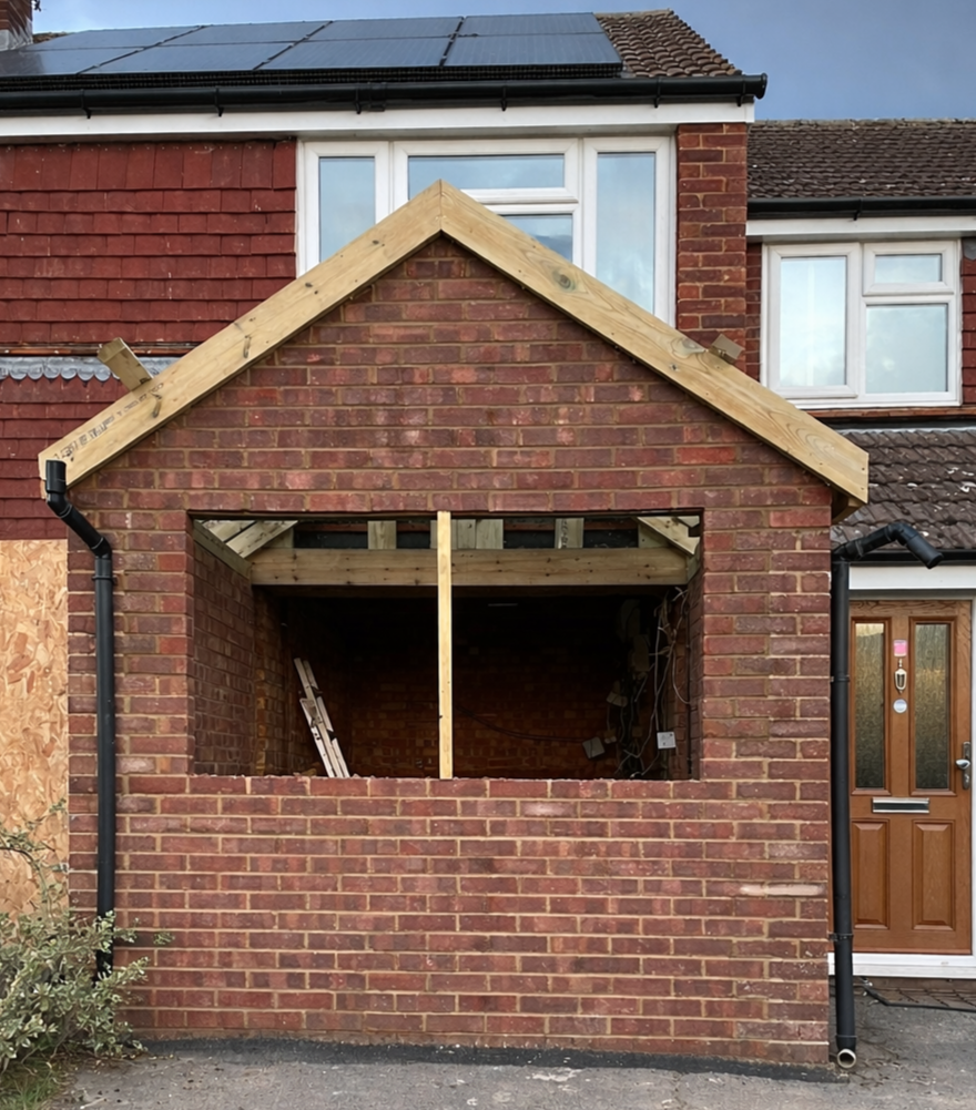 Front view of a house undergoing construction, with an unfinished brick extension or porch area.