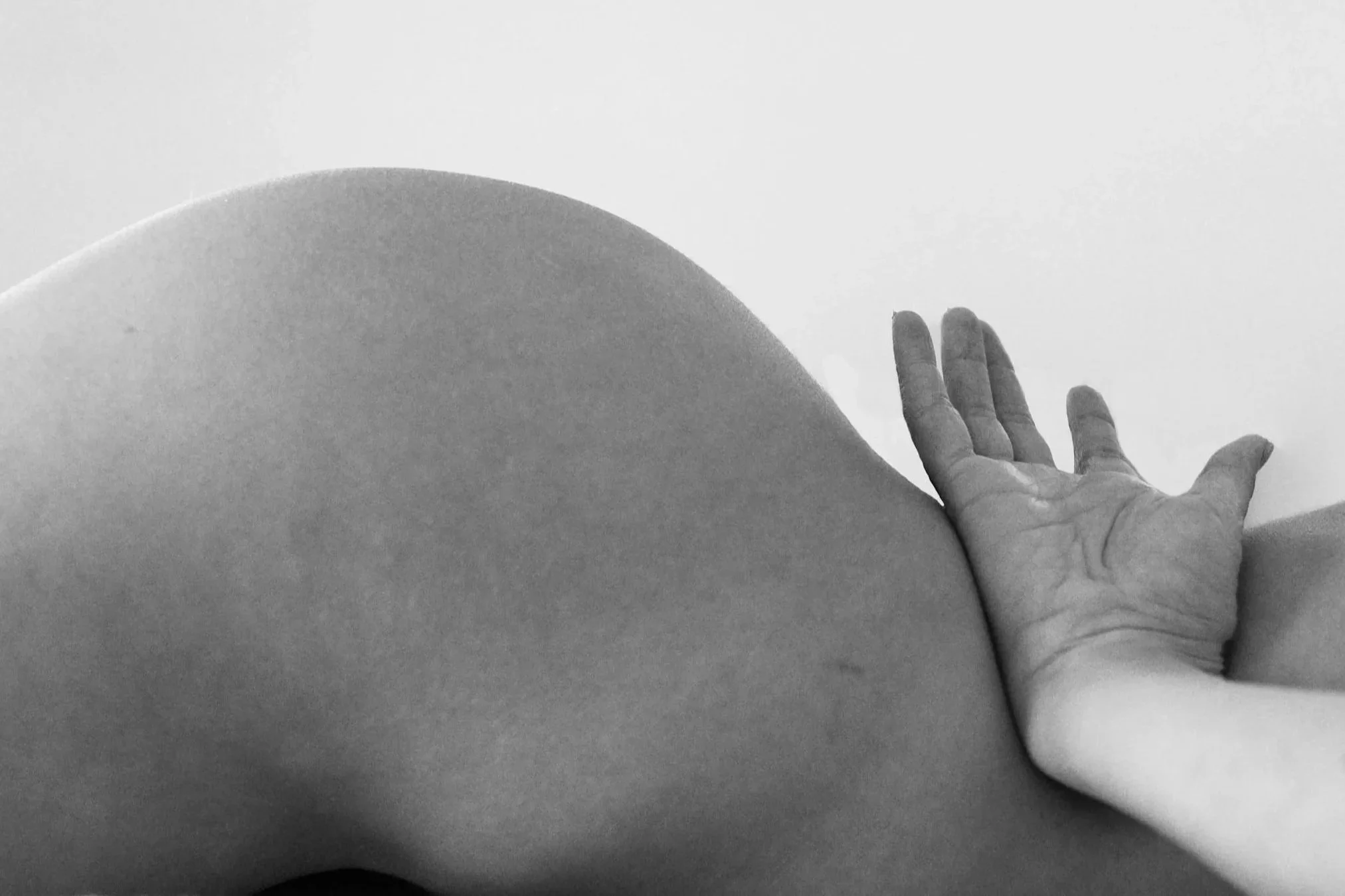 Black and white photograph of a person's hand resting on the side of their body, with a visible curve of the back and shoulder.