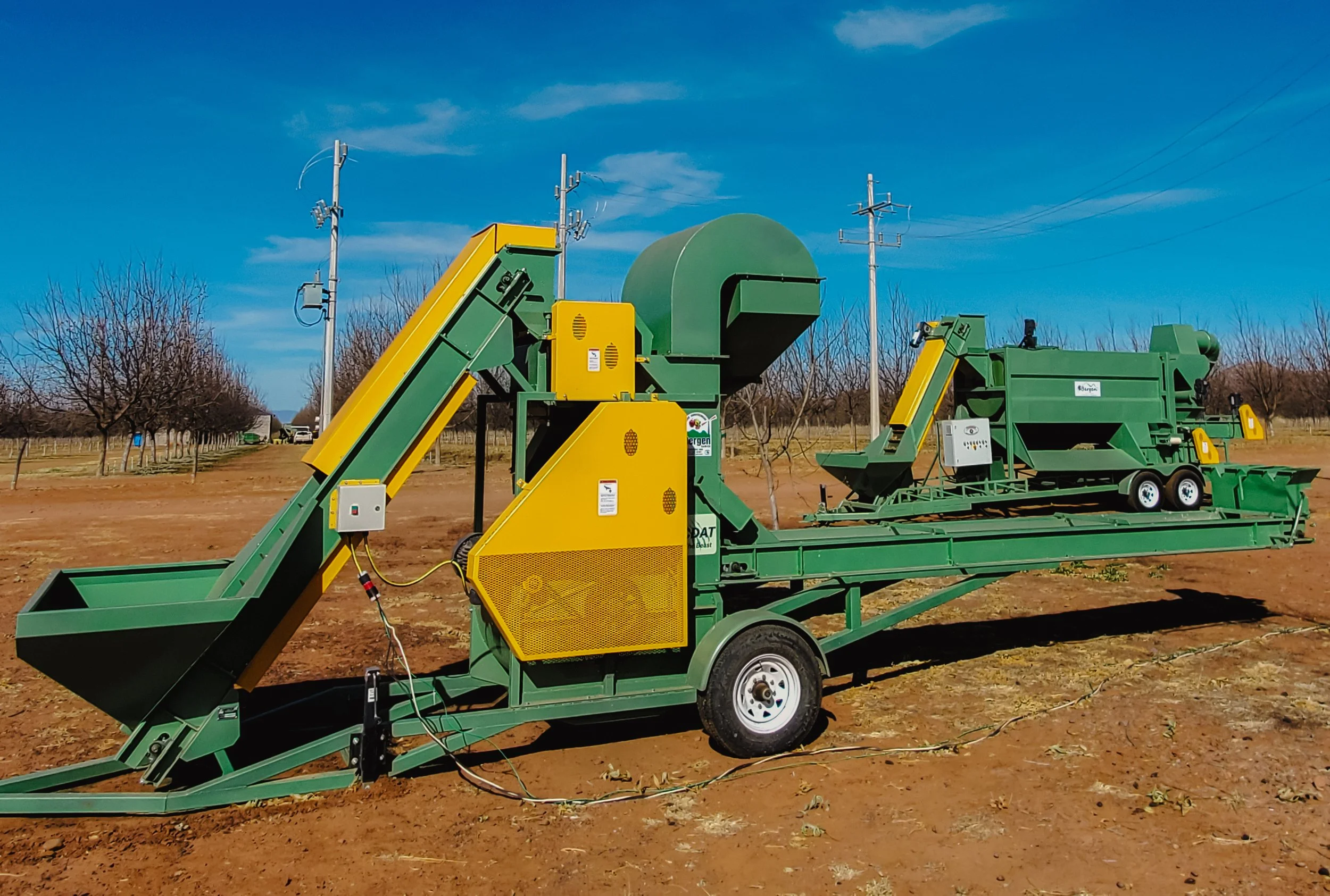 Agricultural machinery in a field, with trees and power lines in the background.