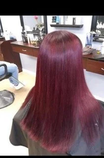 Back view of a woman with long, straight, burgundy-colored hair inside a salon.