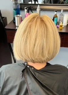 Back of a person's head with a blonde bob haircut sitting in a salon chair, surrounded by salon tools.