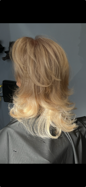 Side view of a woman's blonde layered hairstyle with curled ends, in a salon setting