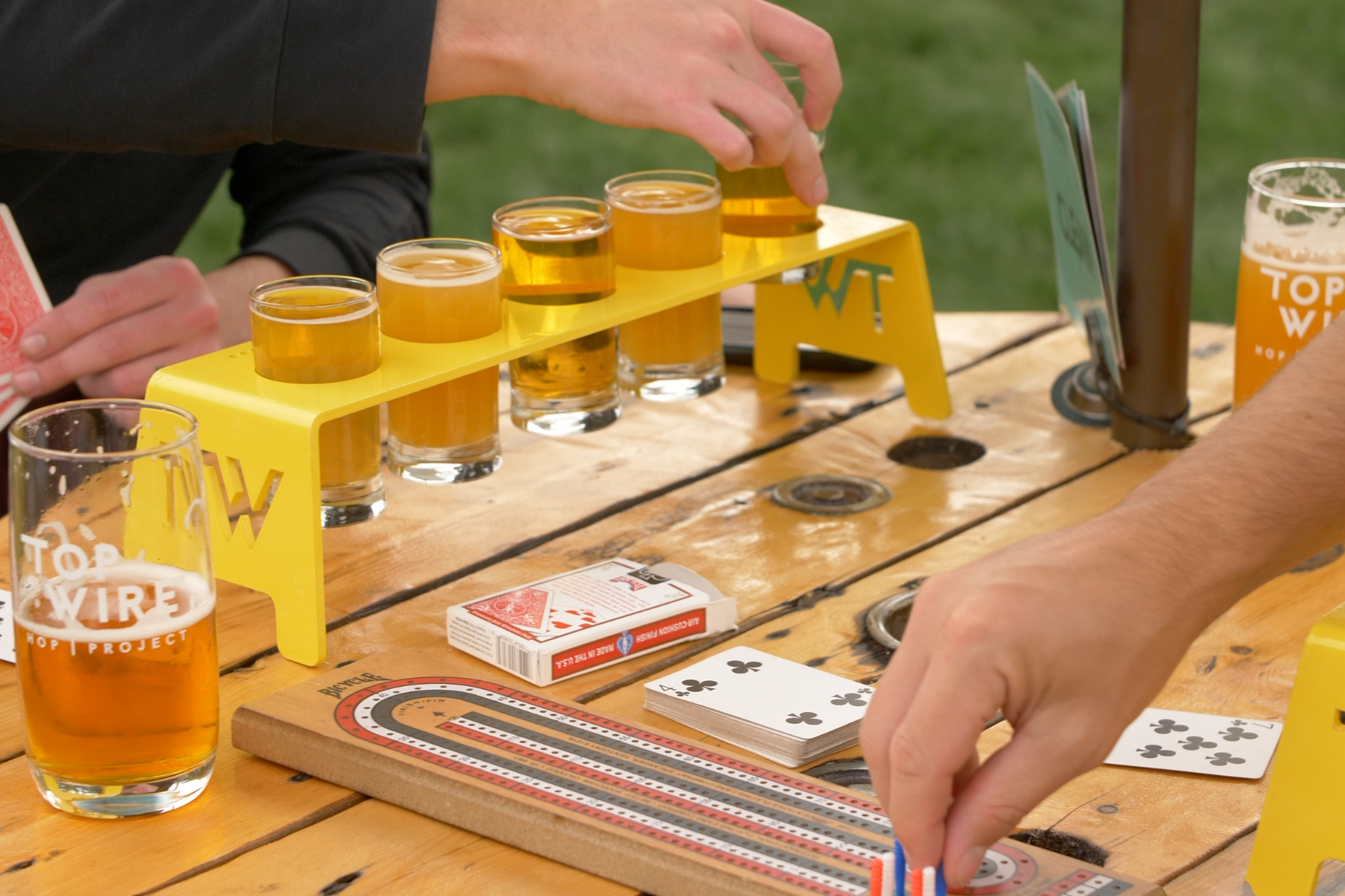 People playing games on a wooden table outdoors while enjoying local craft beer.