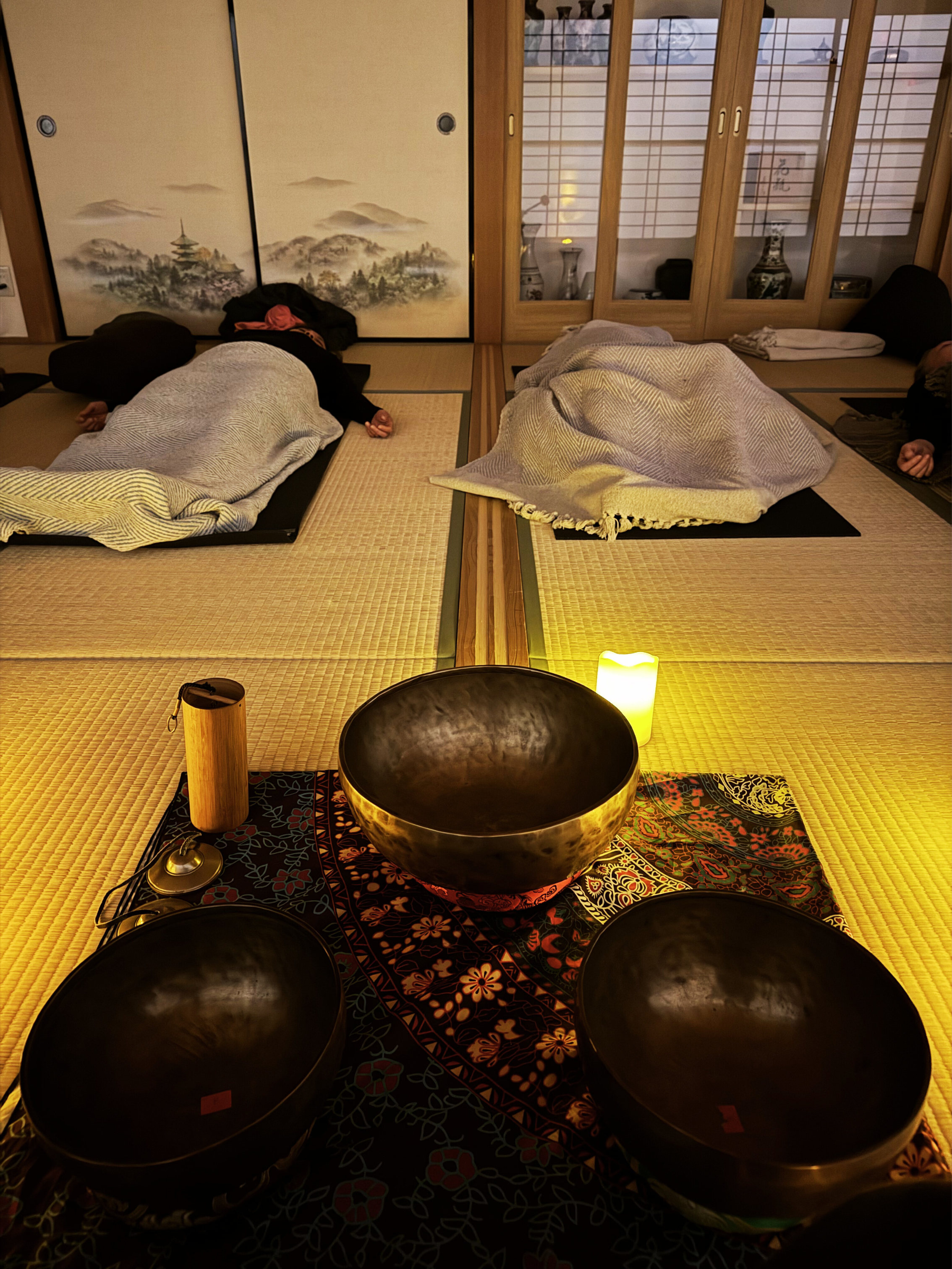 People lying on tatami mats during a sound healing session with singing bowls and a lit candle in a traditional Japanese room.