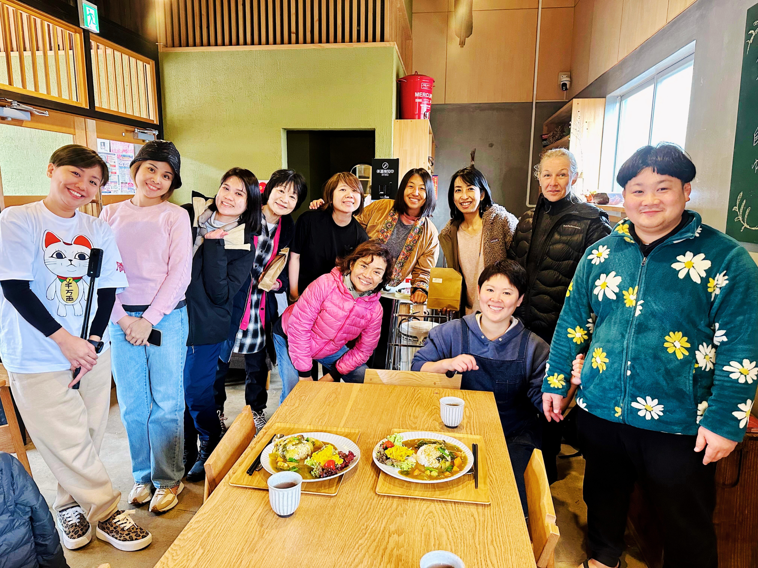 Group of people gathered around a table with two plates of food in a cozy restaurant or cafe, smiling and posing for the photo.