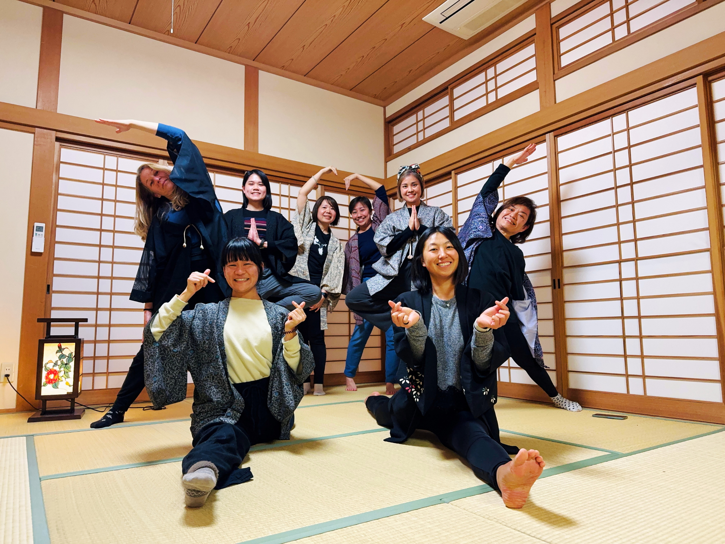 Group of women in traditional Japanese clothing posing and smiling in a tatami room with wooden sliding doors.