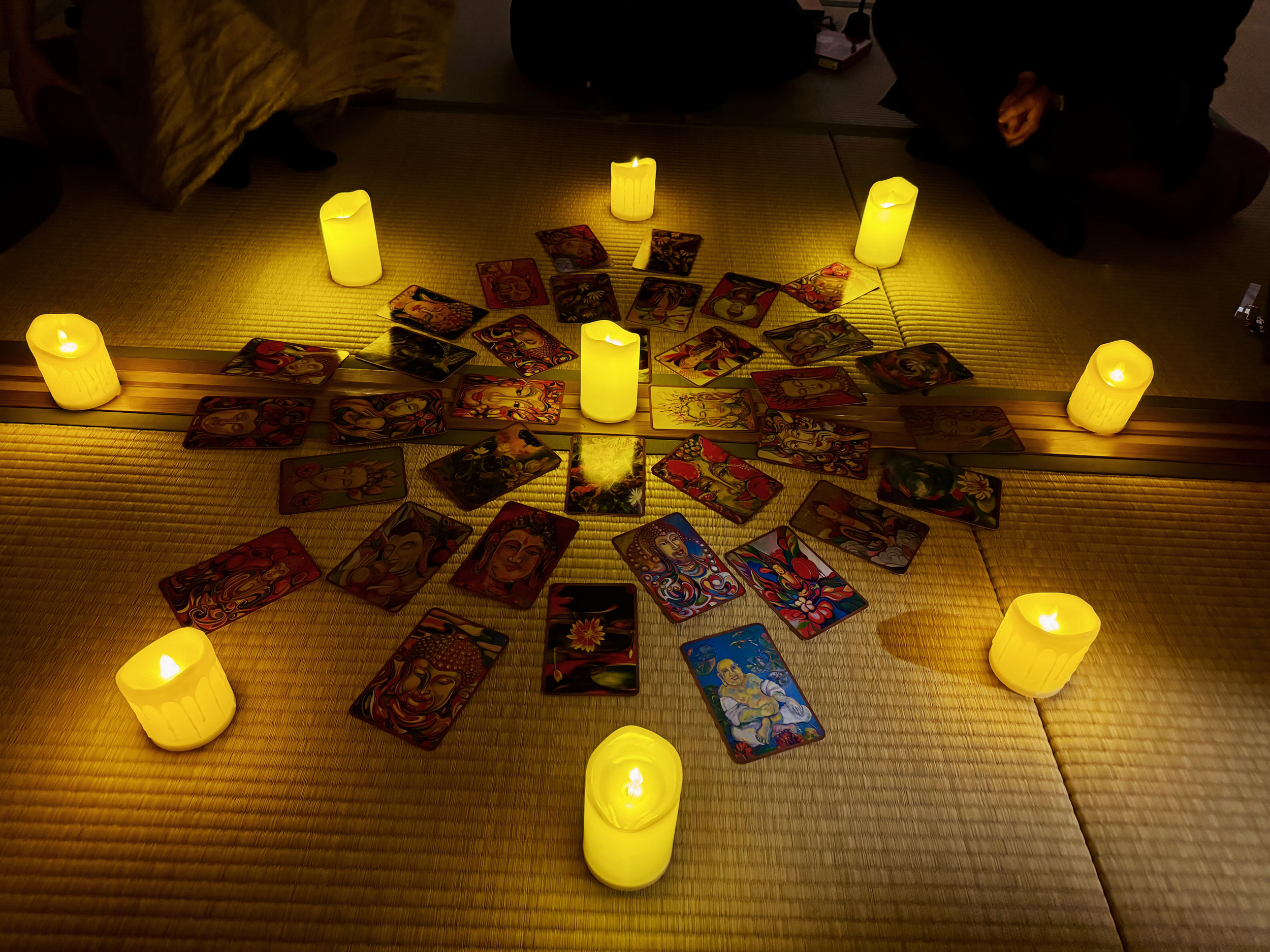 Tarot cards arranged in a circular pattern on a tatami mat, illuminated by candles.