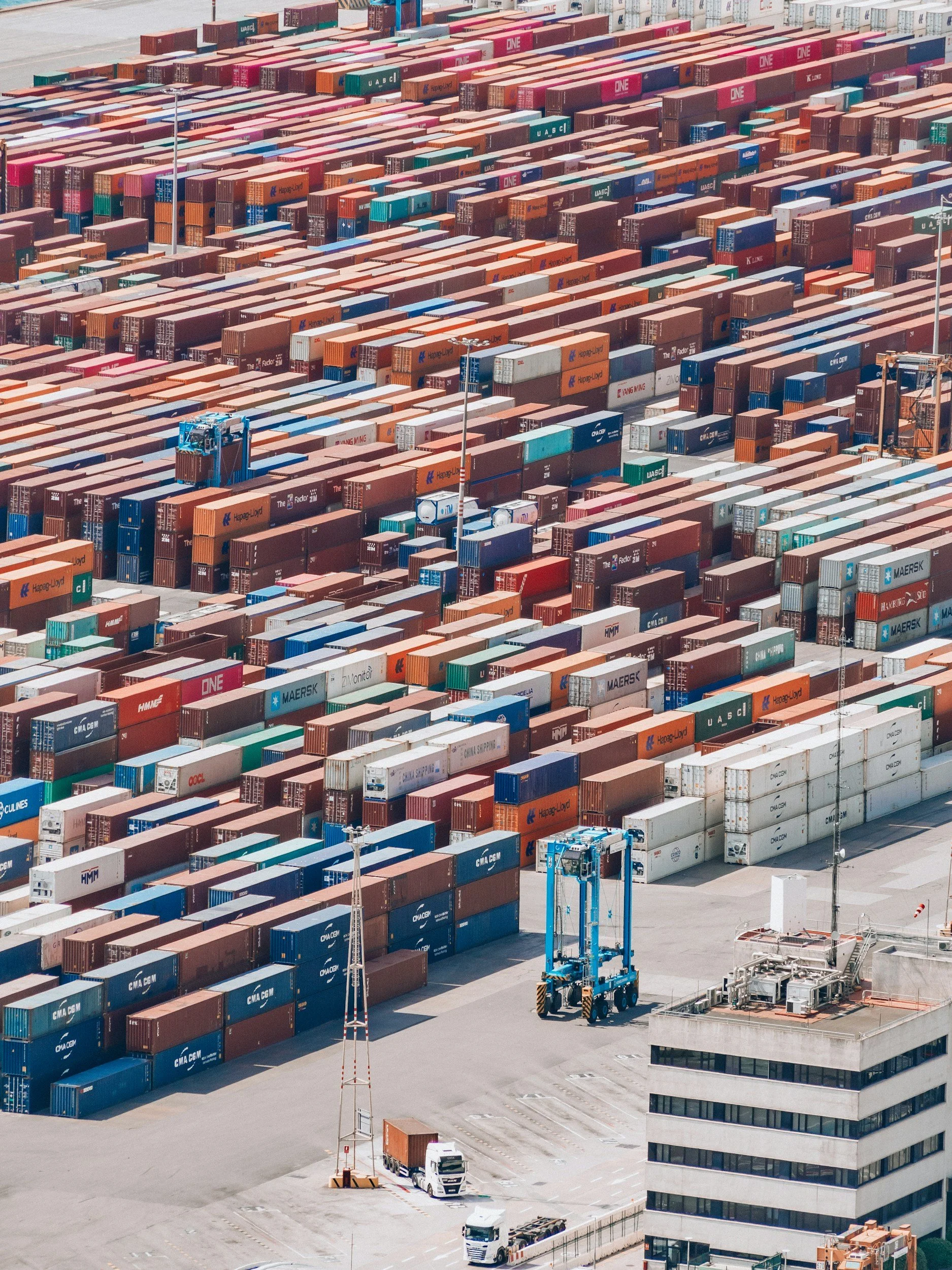 Aerial view of a large container yard with numerous colorful shipping containers and a few trucks and cranes.