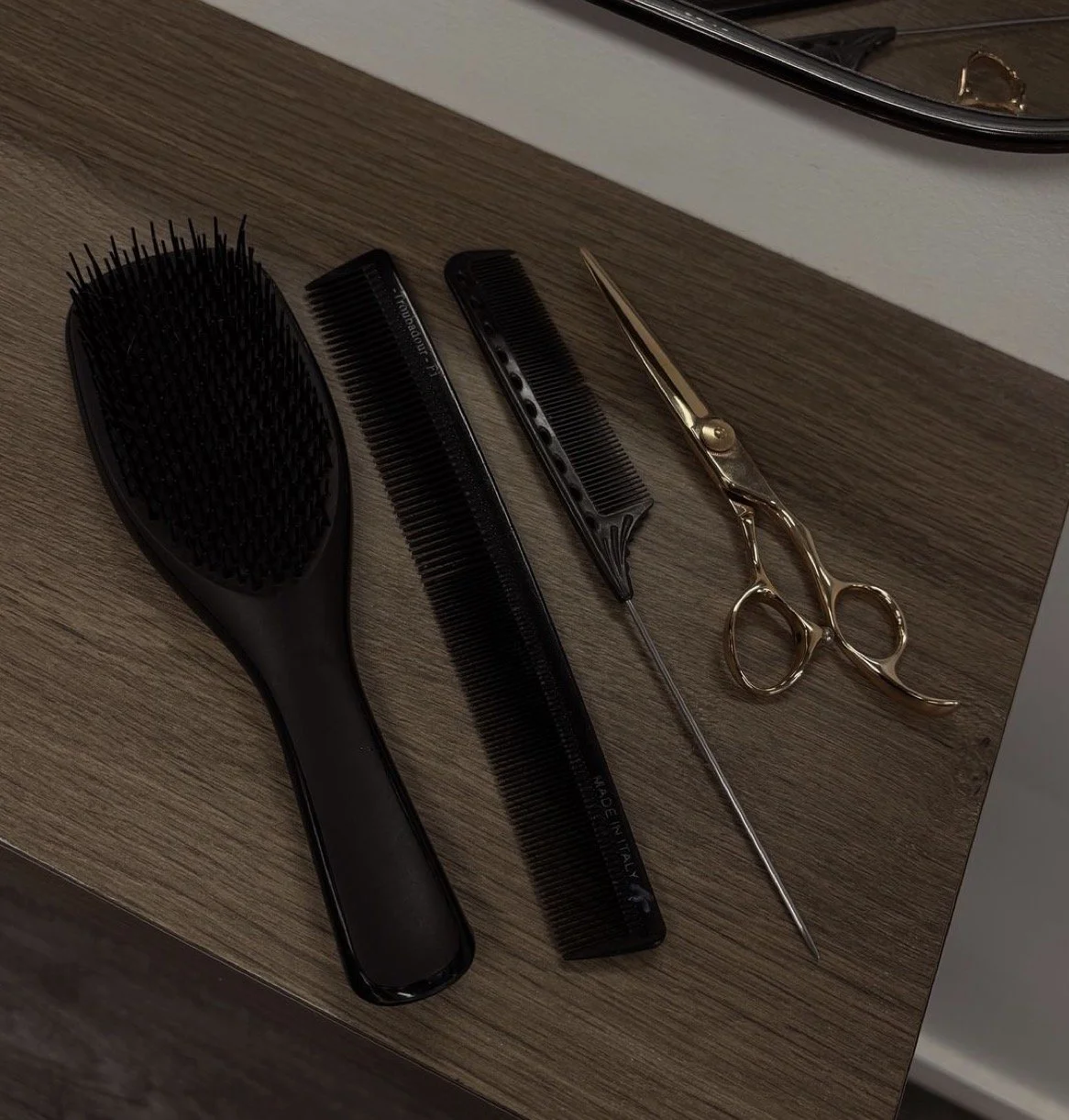 Hairbrush, two combs, and scissors on a wooden surface in front of a mirror.