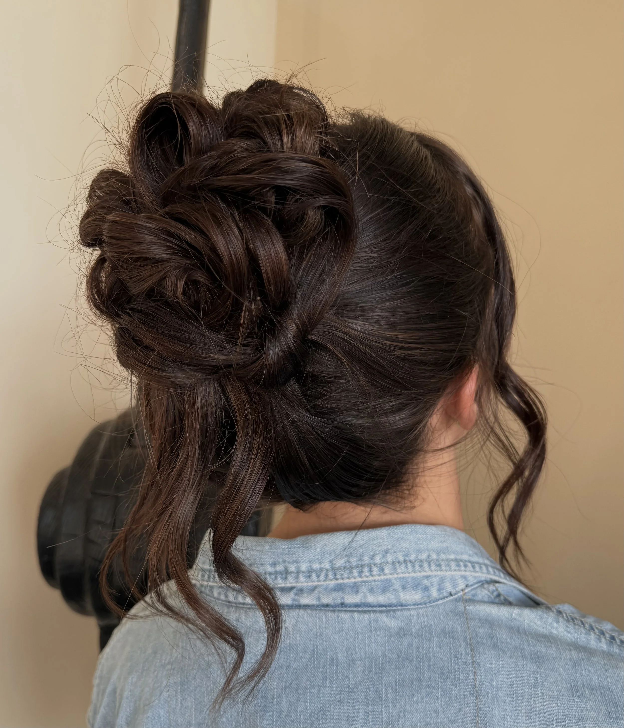 Woman with brown hair styled in an intricate updo with curls, wearing a denim jacket