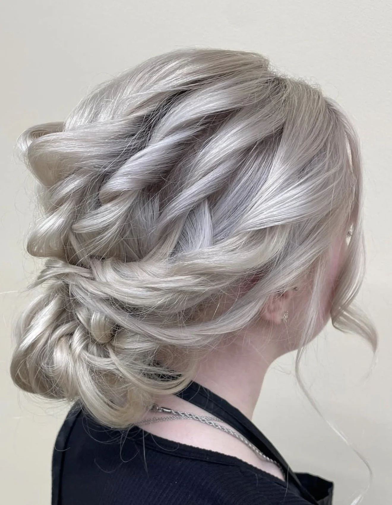 Side view of a person with platinum blonde, loosely curled hair styled in a messy updo.