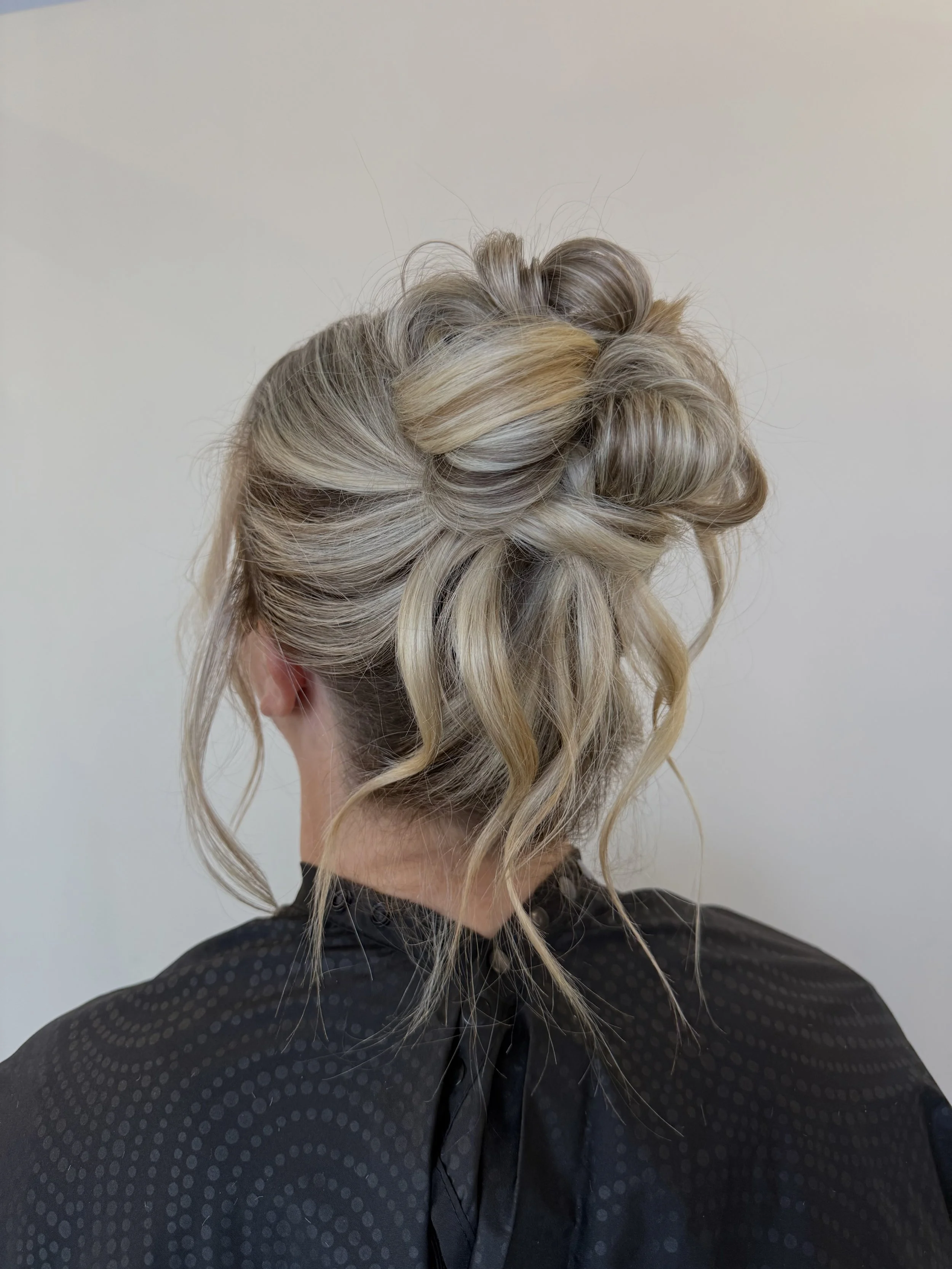 Back view of a woman with an elegant blonde updo hairstyle, wearing a black cape.