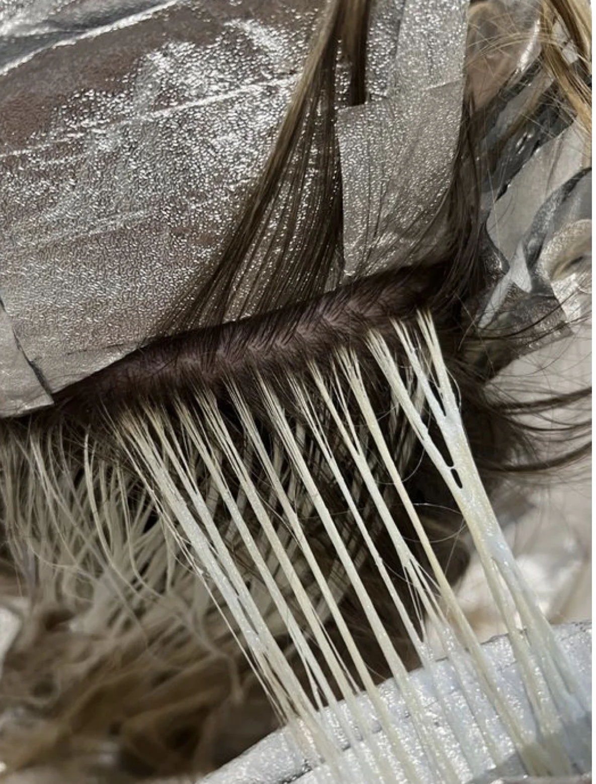 Close-up of hair extensions with tape, showing the wefts and strands of hair being separated during a hair extension application.
