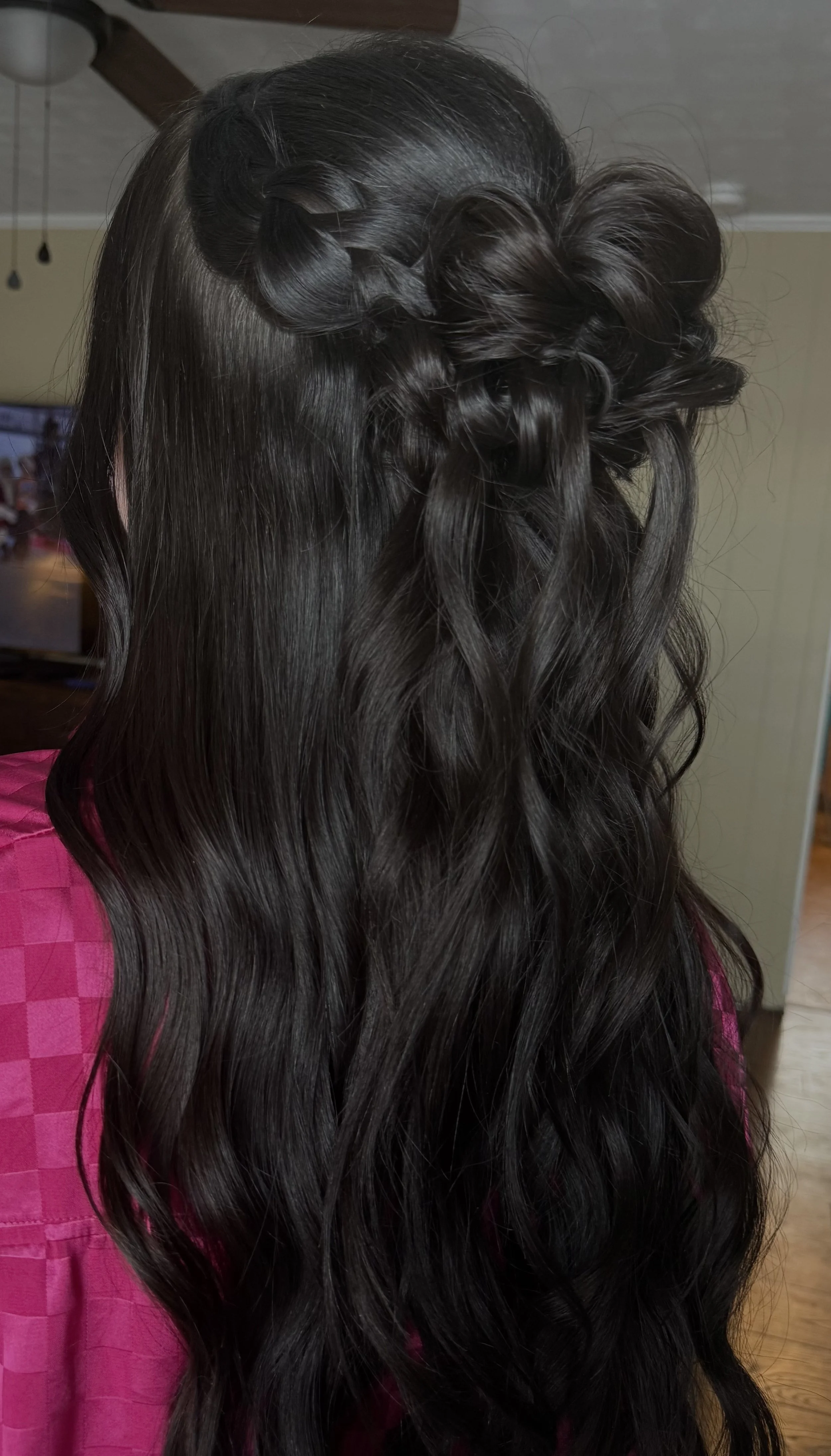 A woman with long dark hair styled with twisted and curled sections on top, and loose wavy hair cascading down.