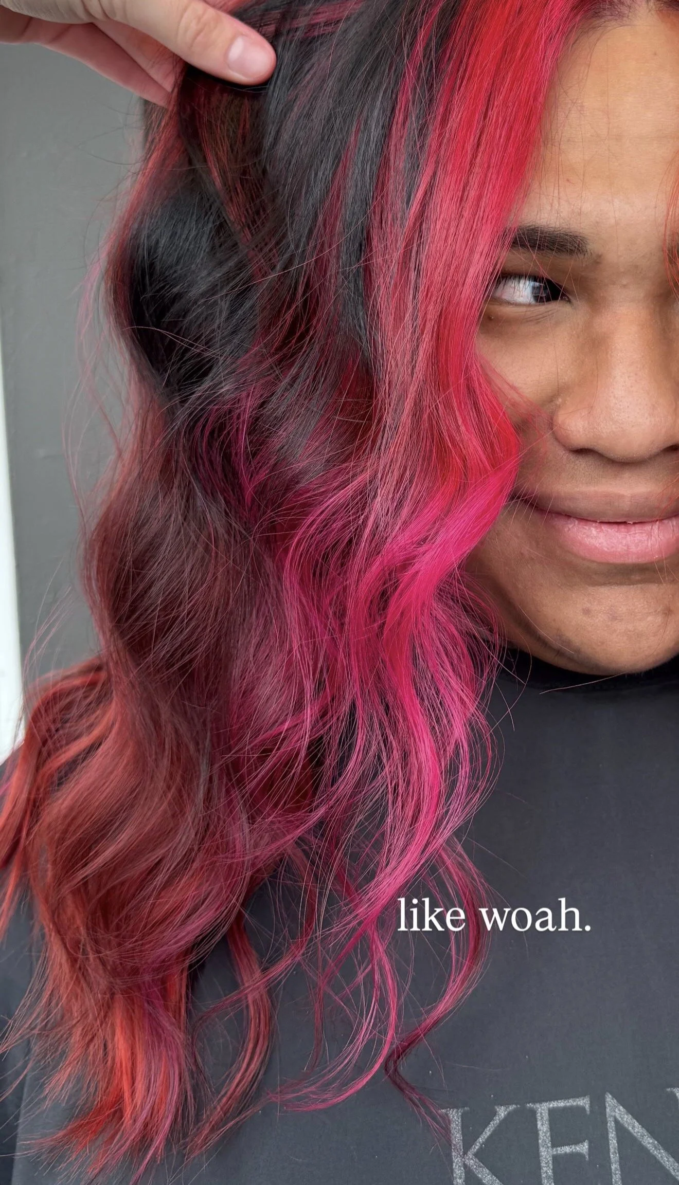 Close-up of a woman with black and hot pink wavy hair, holding a section of her hair, with the text 'like woah.' at the bottom.