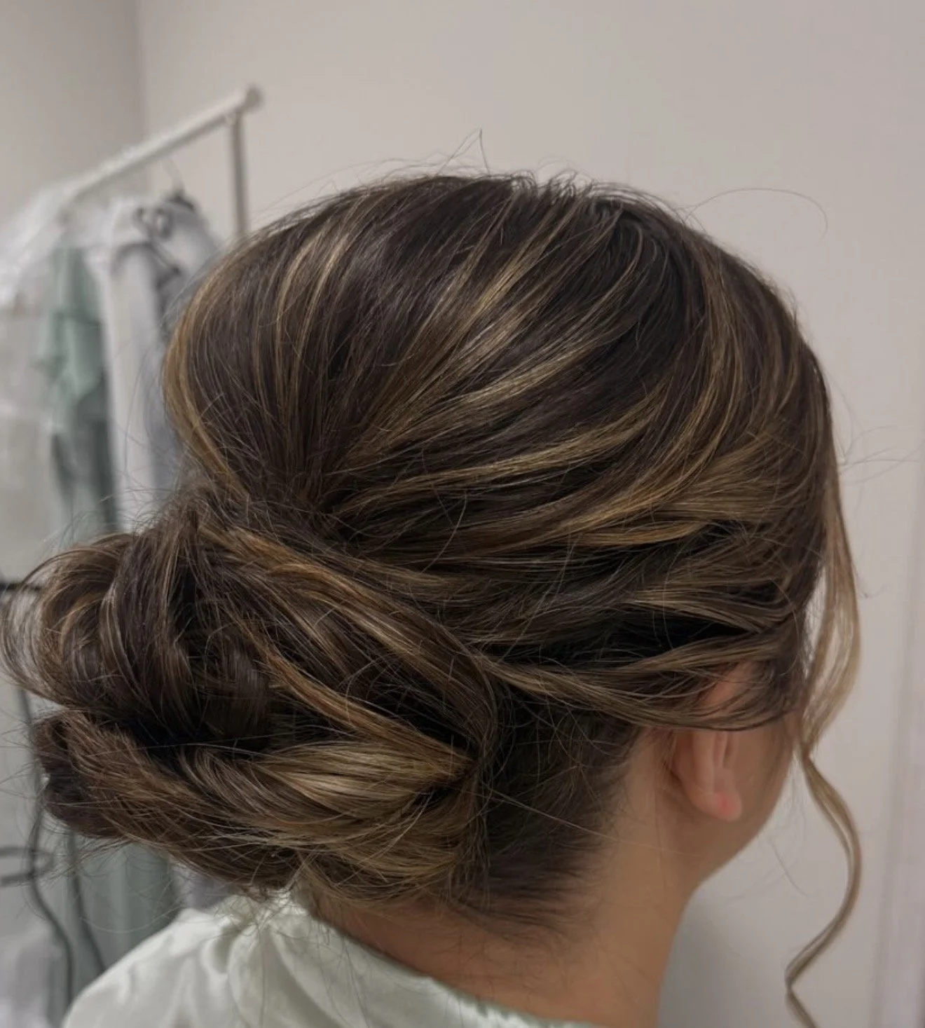 Woman with styled updo hairstyle with blended brown and blonde highlights in a salon setting.
