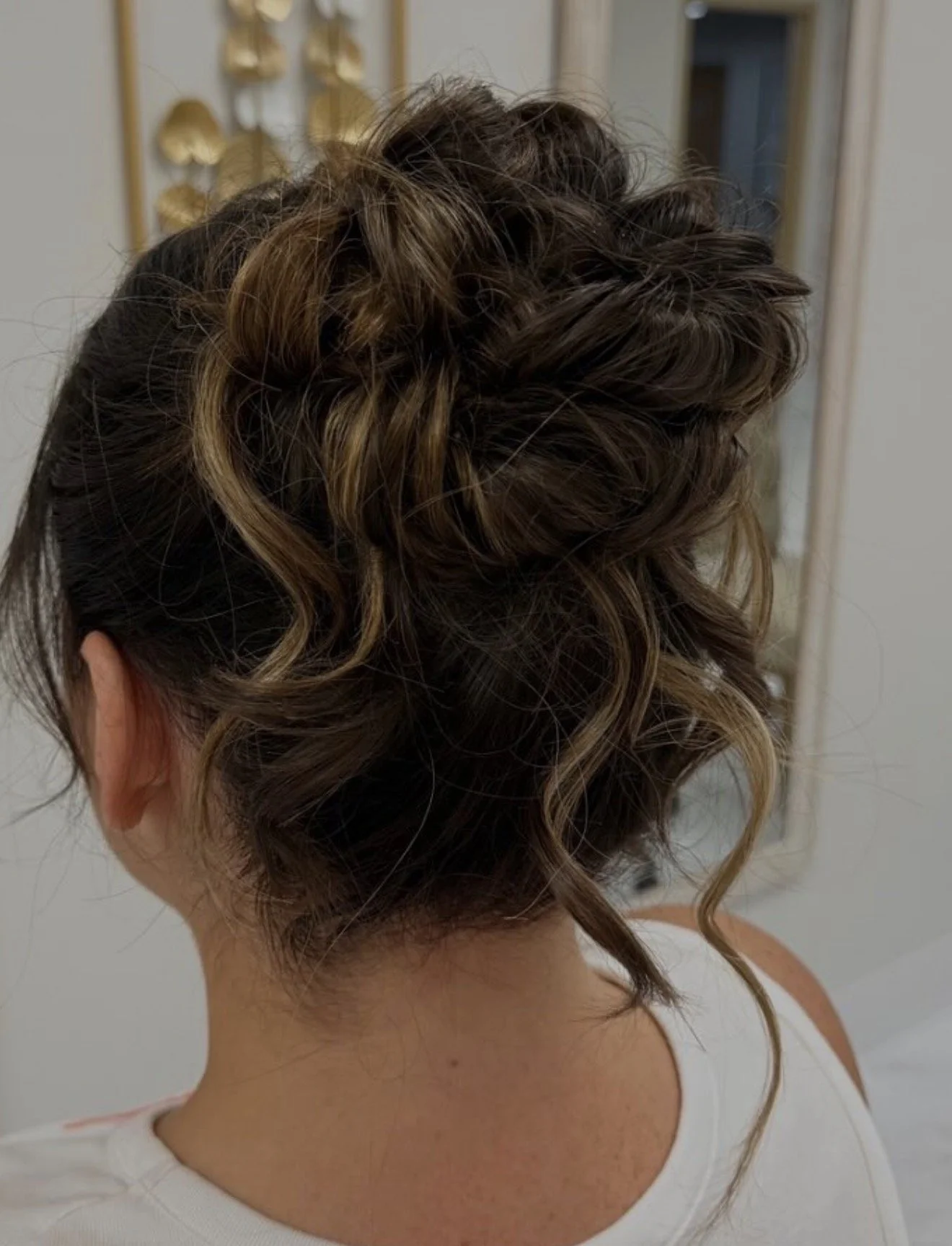 Back of a woman's head showing an intricate updo hairstyle with curls and blonde highlights.