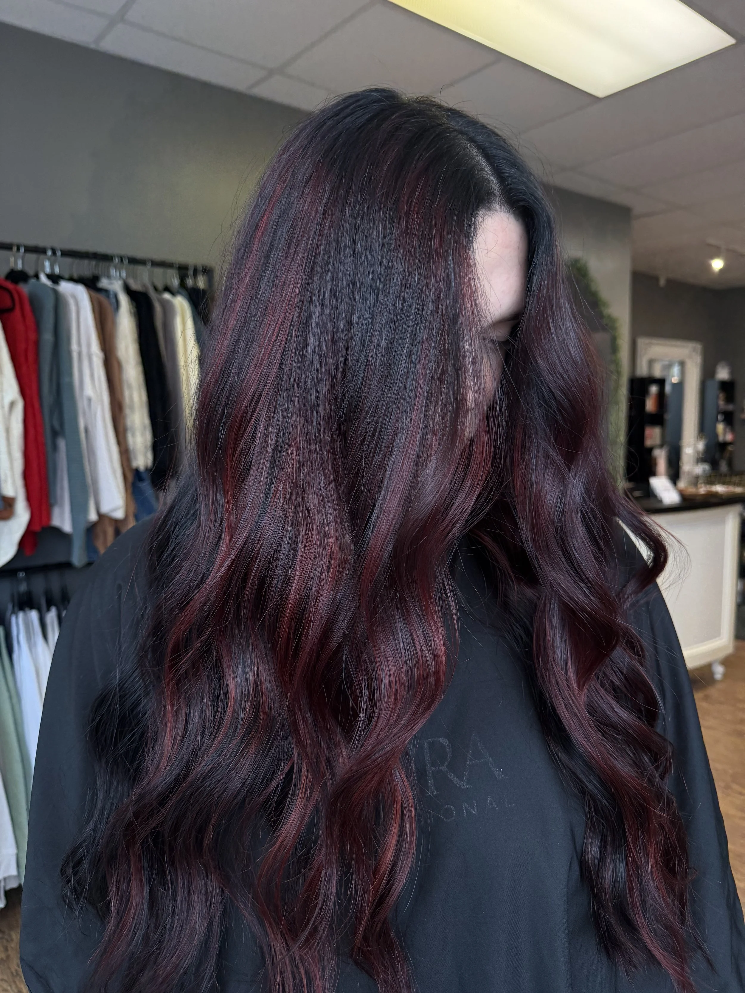A woman with long, wavy burgundy hair standing inside a clothing store.