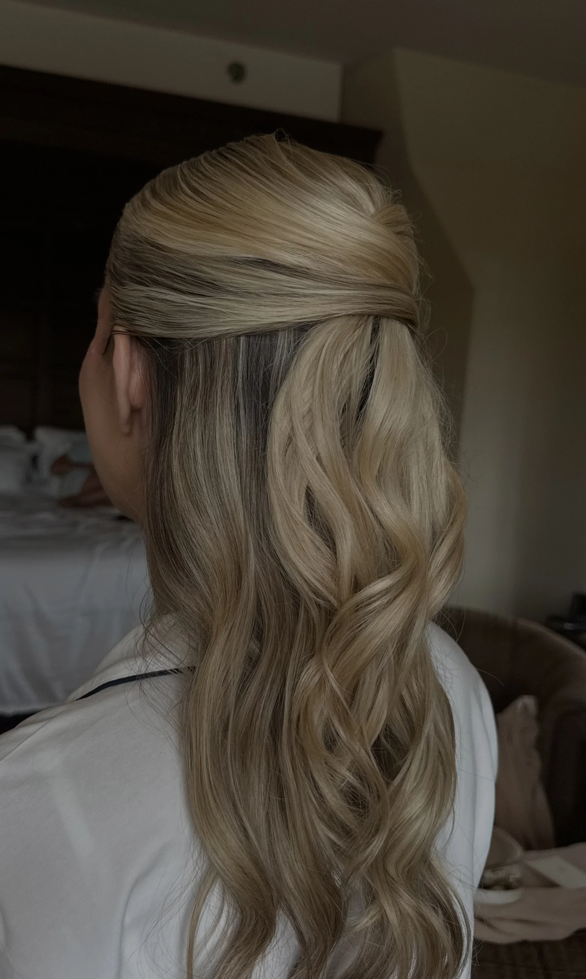 Back view of a woman with long, wavy blonde hair styled with a twist at the top.