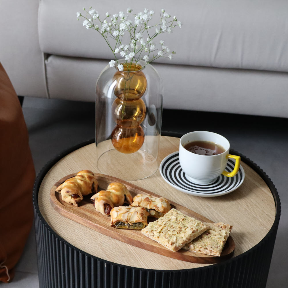 Tazza di tè con biscotti e dolci su un tavolino, decorato con un vaso di fiori bianchi.