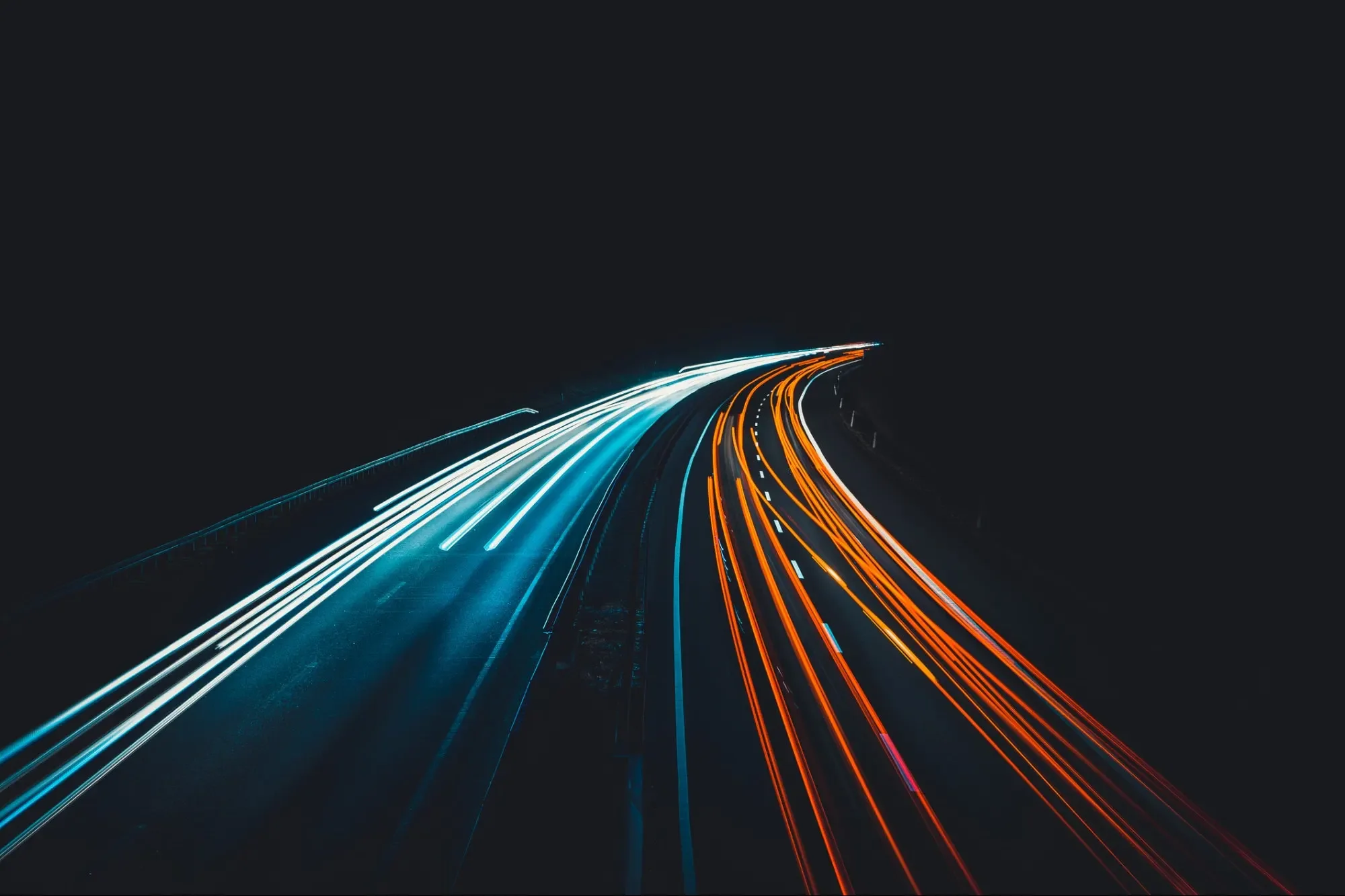 Nighttime highway with streaks of white and orange light trails from moving vehicles, curving into the distance.