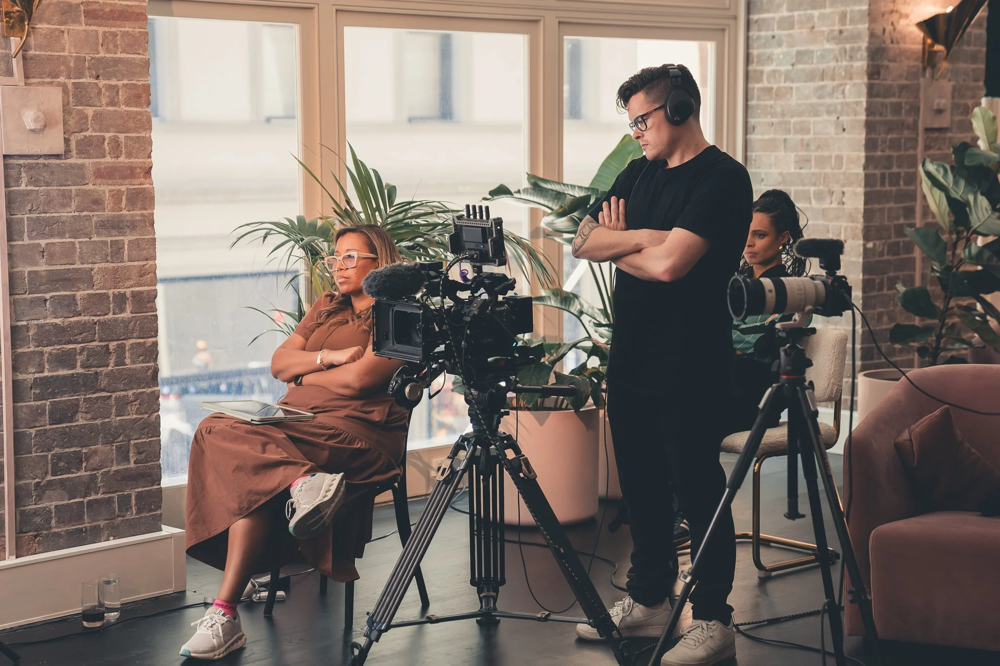 Filmmaker preparing a scene with Marti Hines, a woman sitting on a chair while crew members work with cameras in a cozy indoor setting.