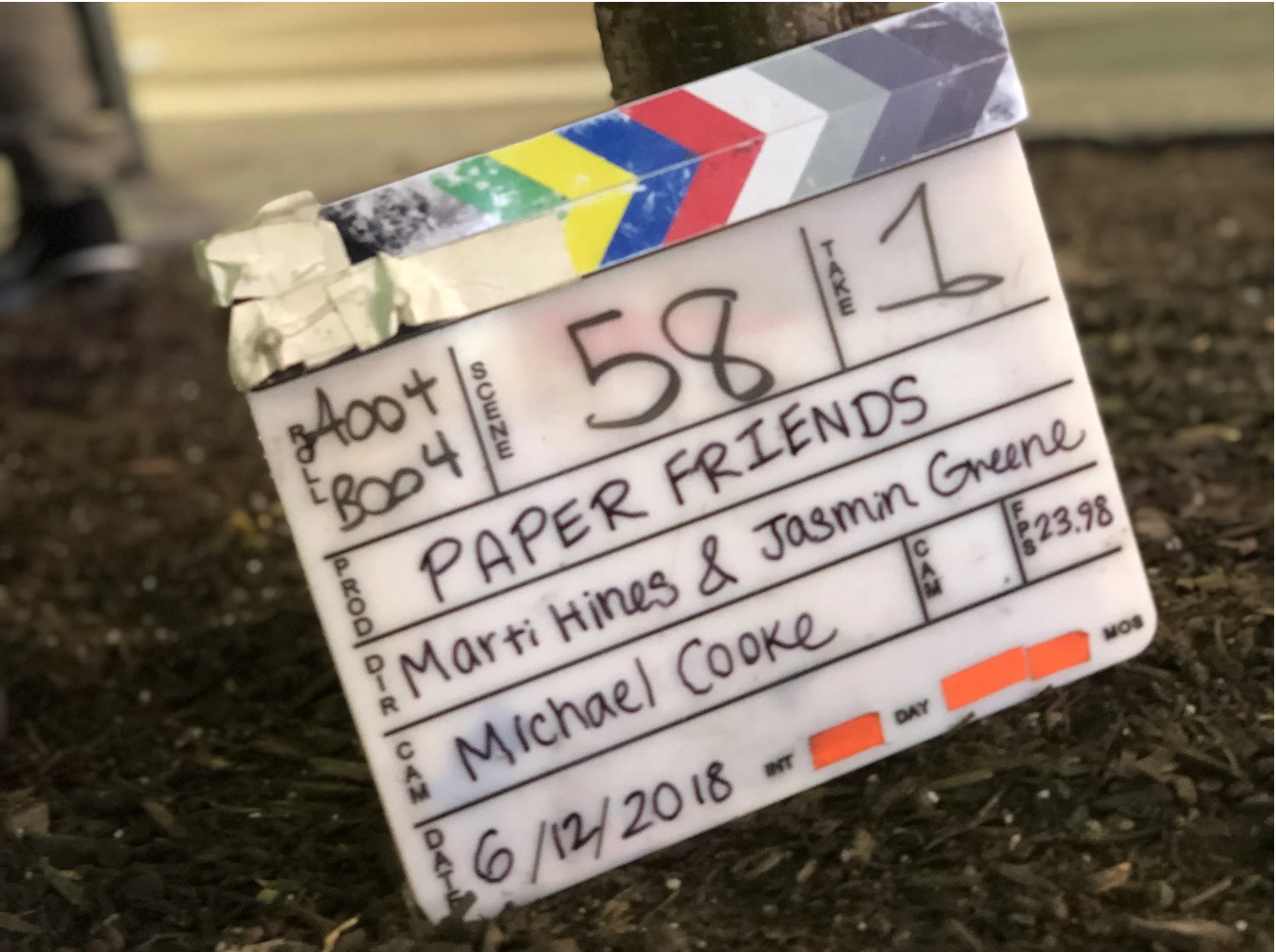 A clapperboard with writing that reads 'Paper Friends' and 'Marti Hines & Jasmin Greene,' the date '6/12/2018,' and the name 'Michael Cooke.'