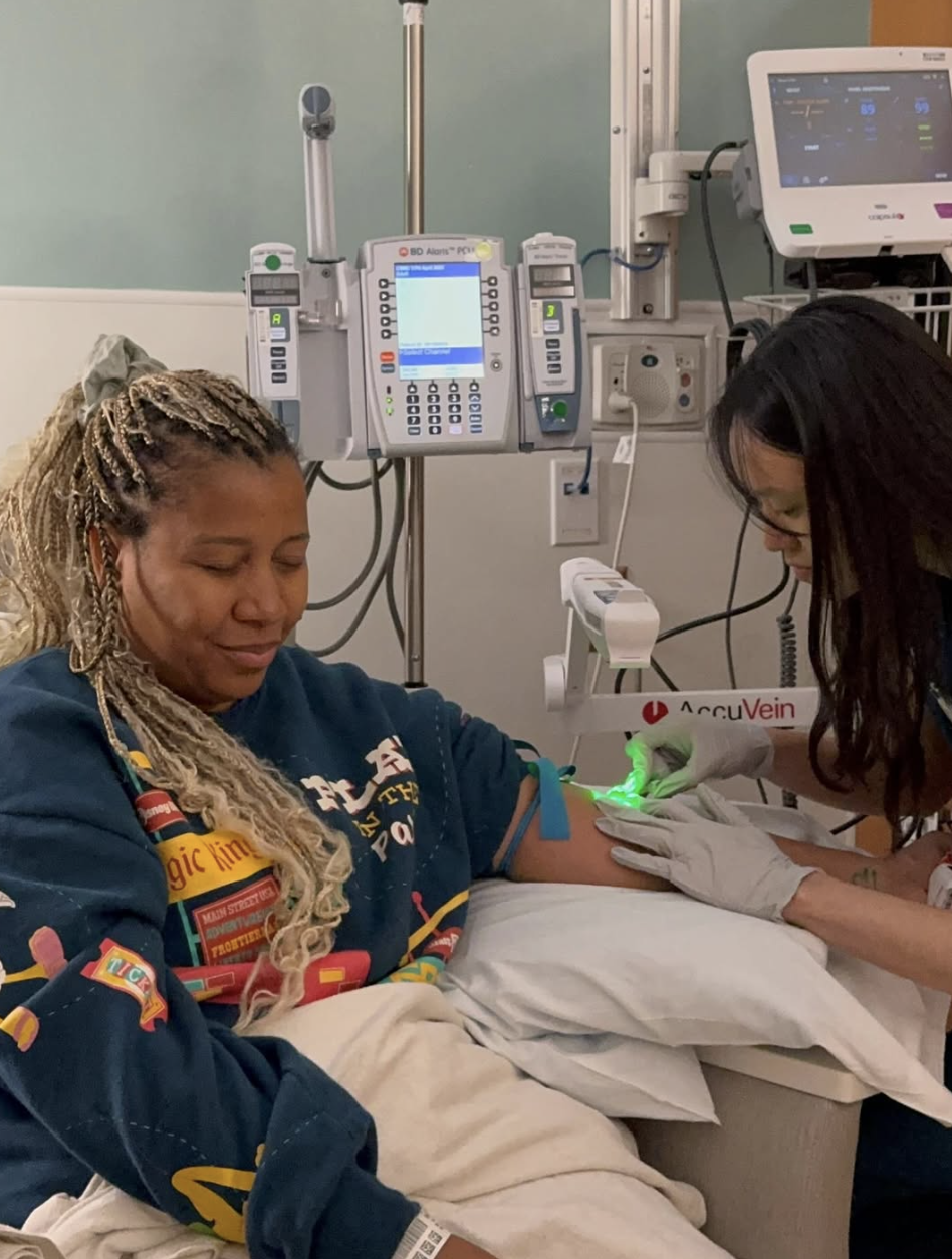 Marti Hines, a woman undergoing a medical procedure for Multiple Sclerosis with a healthcare professional, in a hospital room with medical equipment.