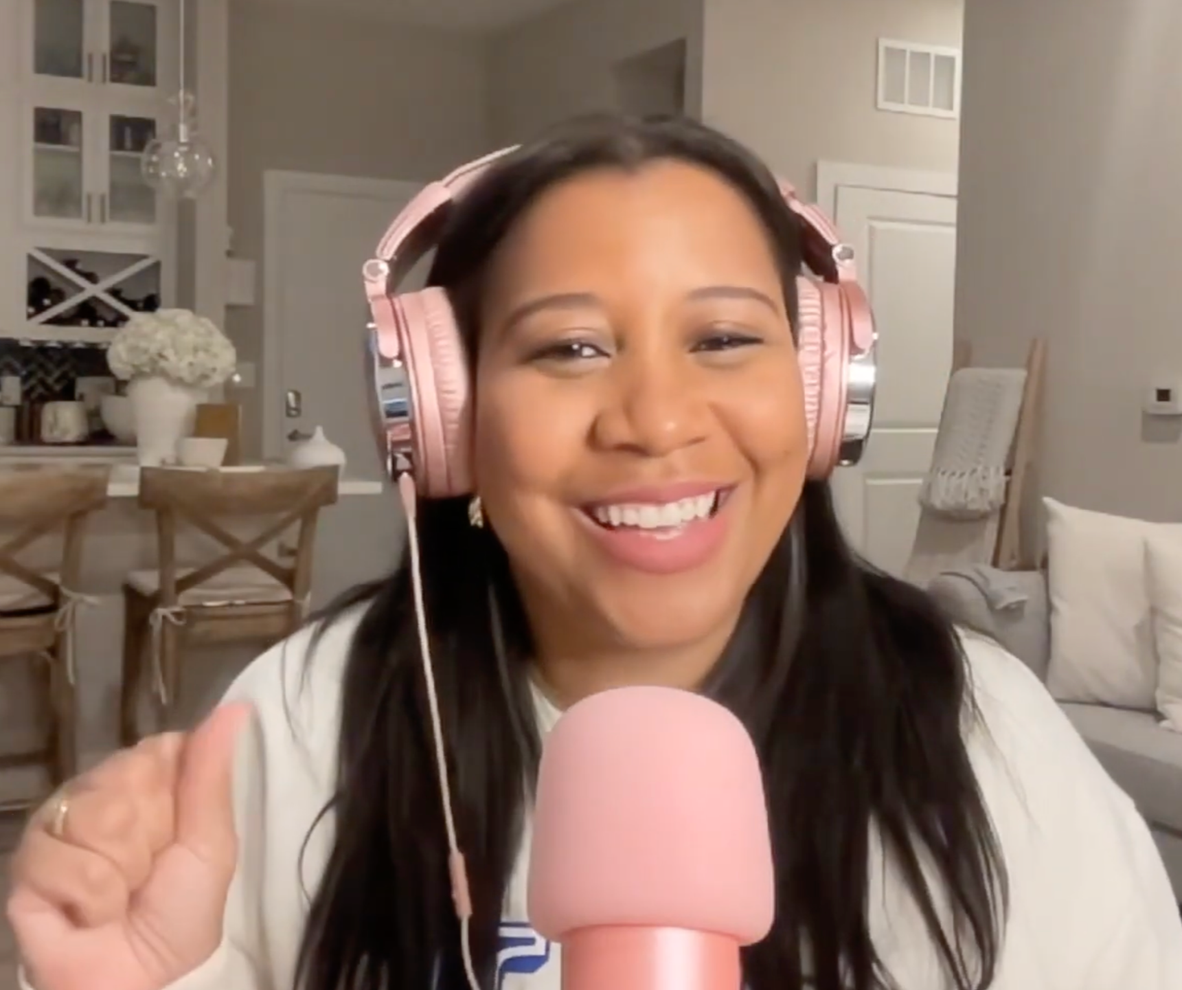 Marti Hines, a woman smiling, wearing pink headphones, speaking into a pink microphone in a cozy home setting.