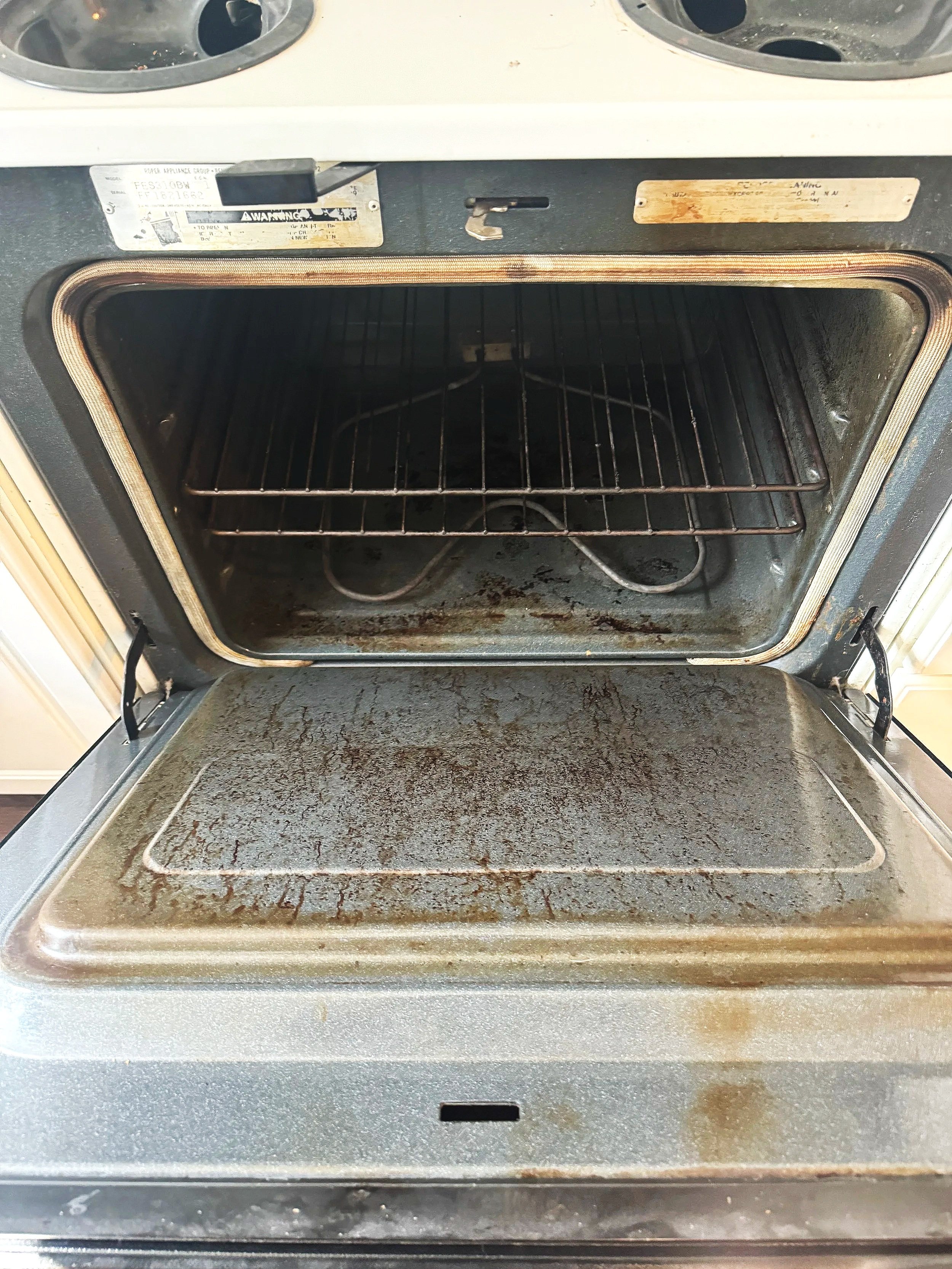 An open oven with a rusty, dirty interior and a metal rack inside.