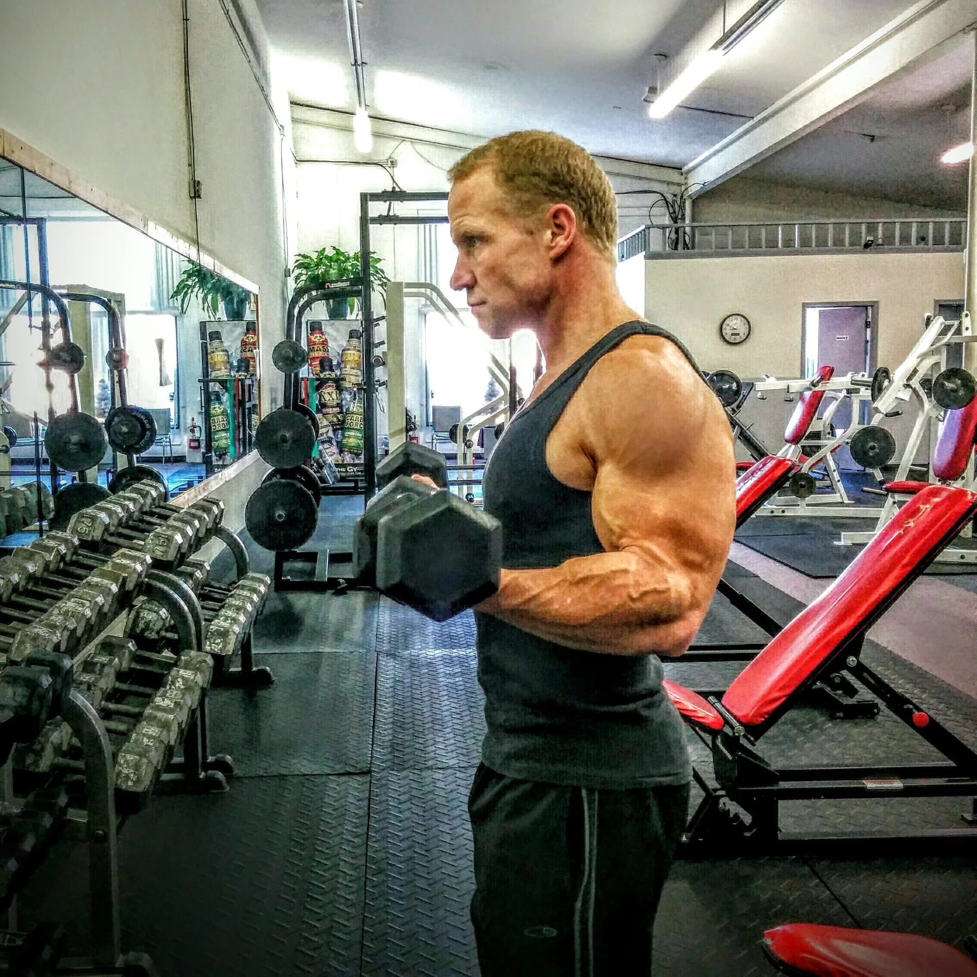 Man lifting a dumbbell in a gym, surrounded by workout equipment and mirrors.
