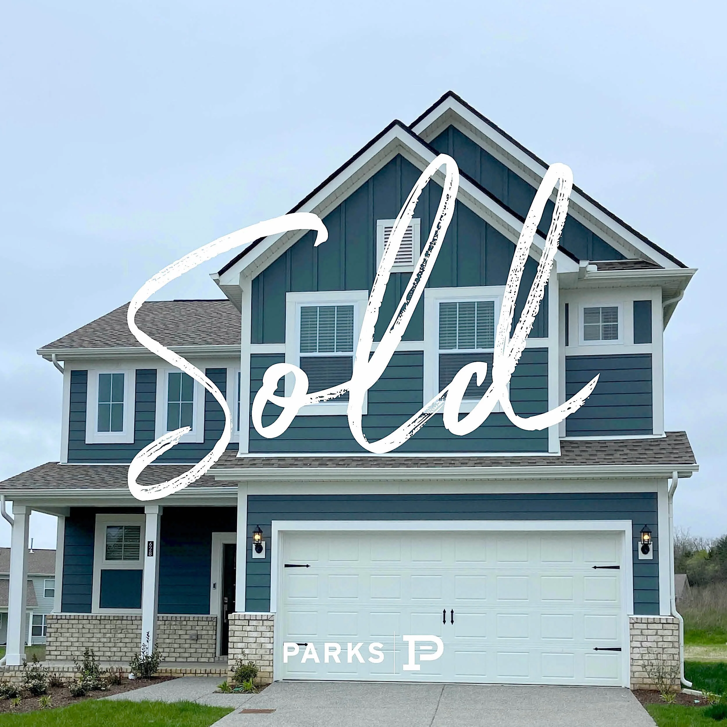 A two-story blue house with white trim, a garage, and front porch, with a grassy yard and brick accents. Overlaid with the words "Sold" in large white cursive and "Parks" with a logo.
