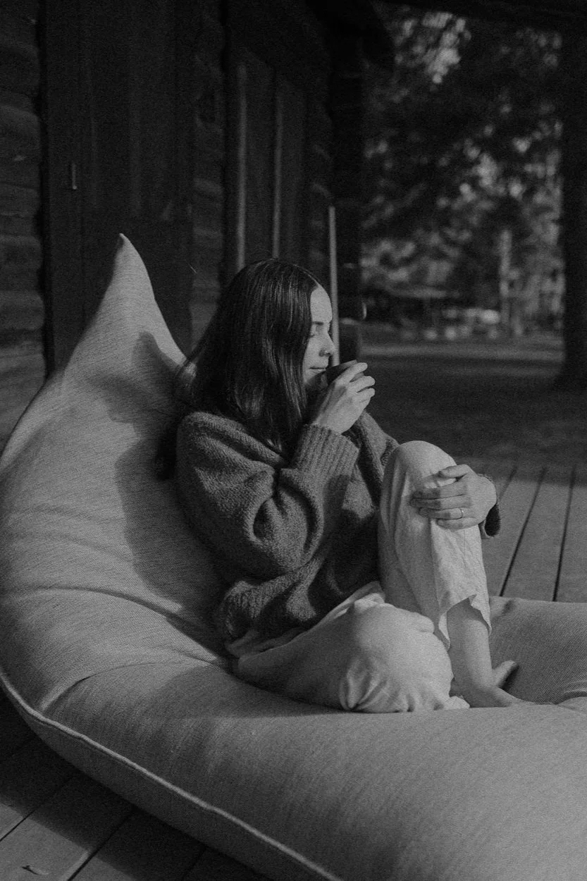 A woman sitting outside on a large cushion, drinking from a cup and thinking, during nighttime.