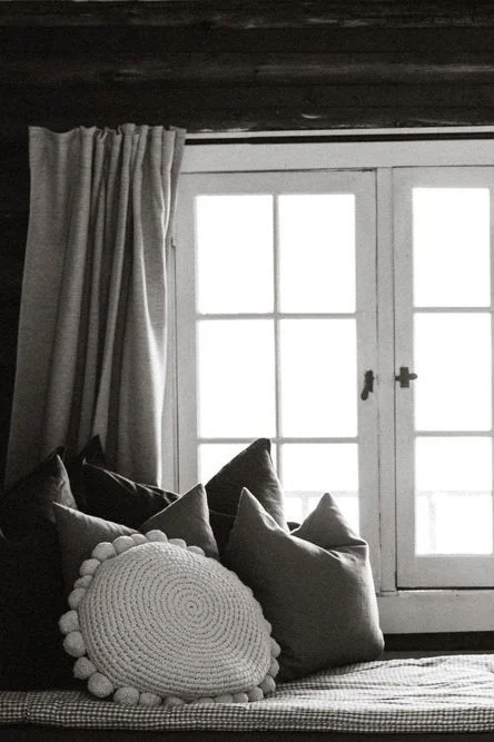 A cozy window seating area with cushions and a curtain, next to a large window.