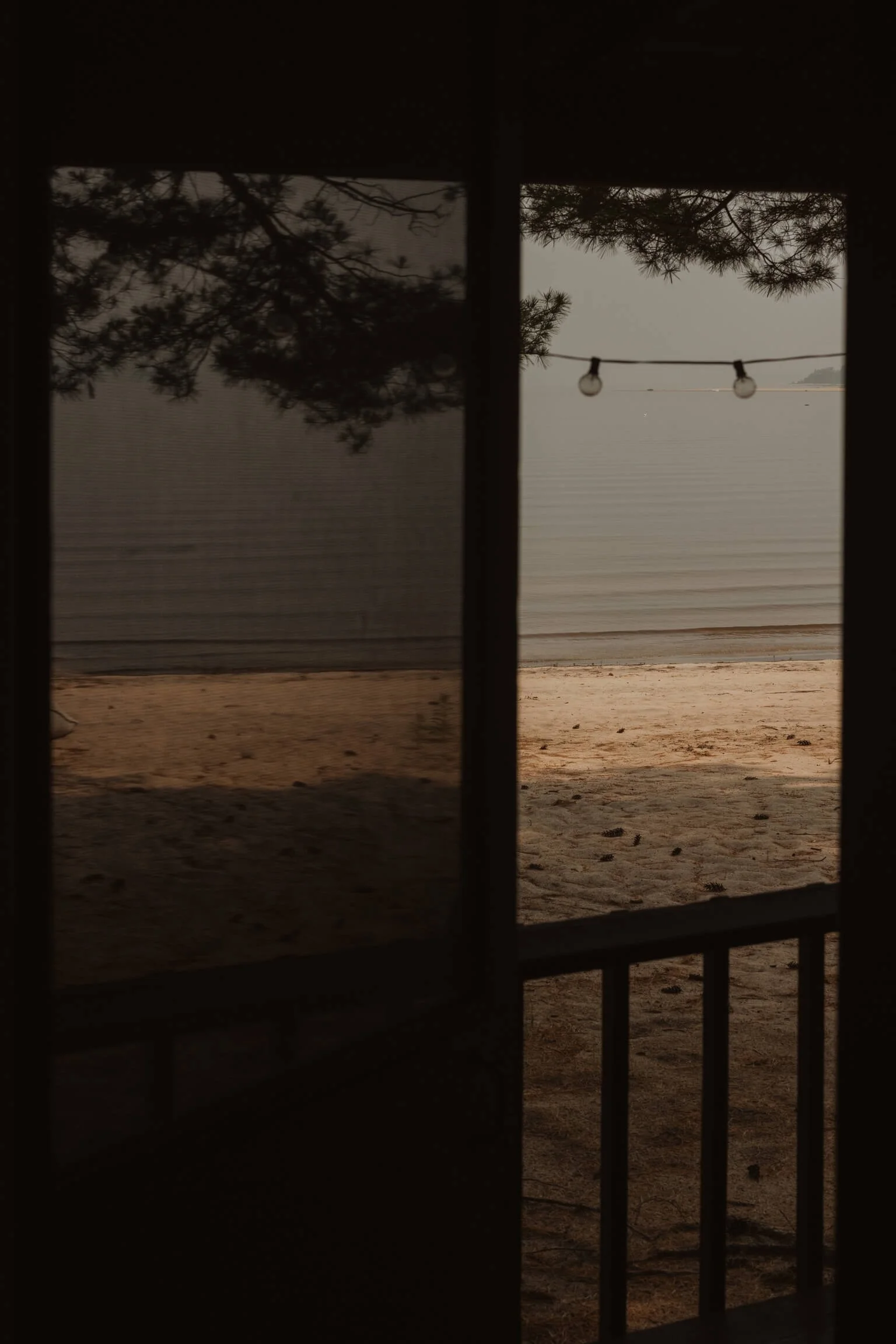 View of a beach seen through a window with a string of lights hanging above the water.
