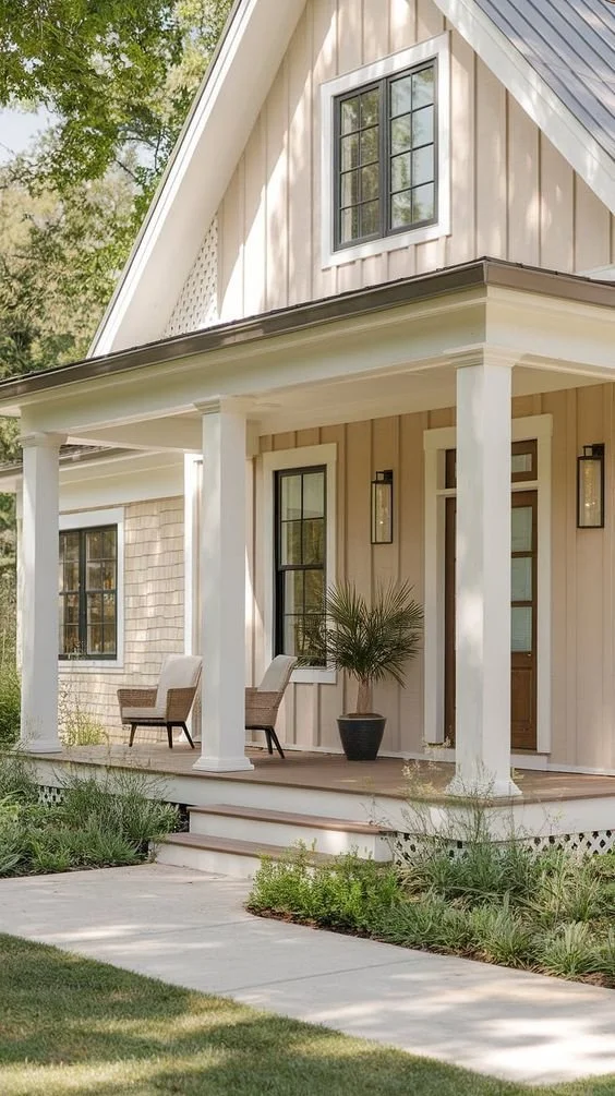 Front porch of a modern house with white pillars, a potted plant, two chairs, and large windows.
