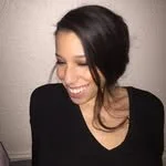 A woman smiling and looking down, wearing a black top with dark hair.