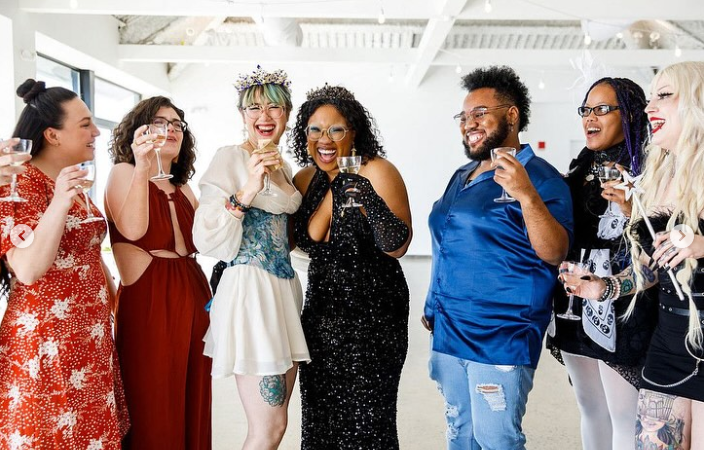 Group of friends celebrating, smiling, holding drinks, in a bright decorated room.