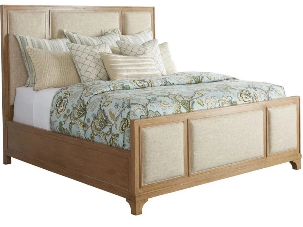 A wooden bed frame with beige upholstered panels and numerous pillows, topped with a floral bedspread.