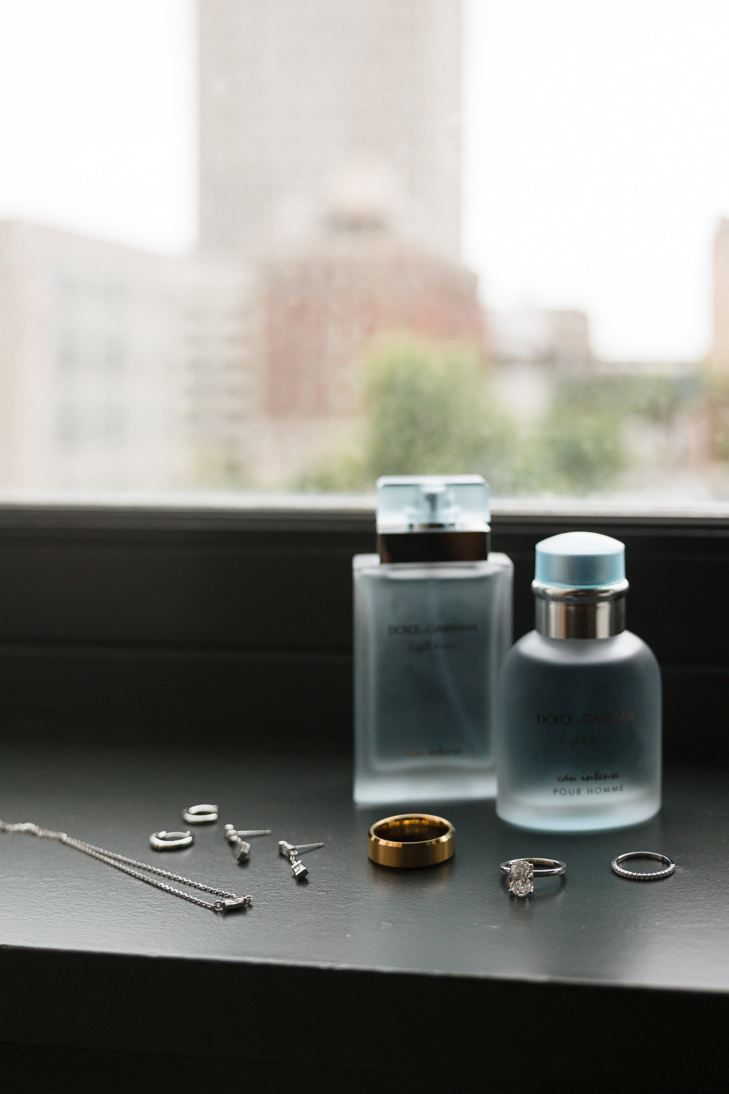 Jewelry and perfume bottles on a windowsill with blurred cityscape in the background.