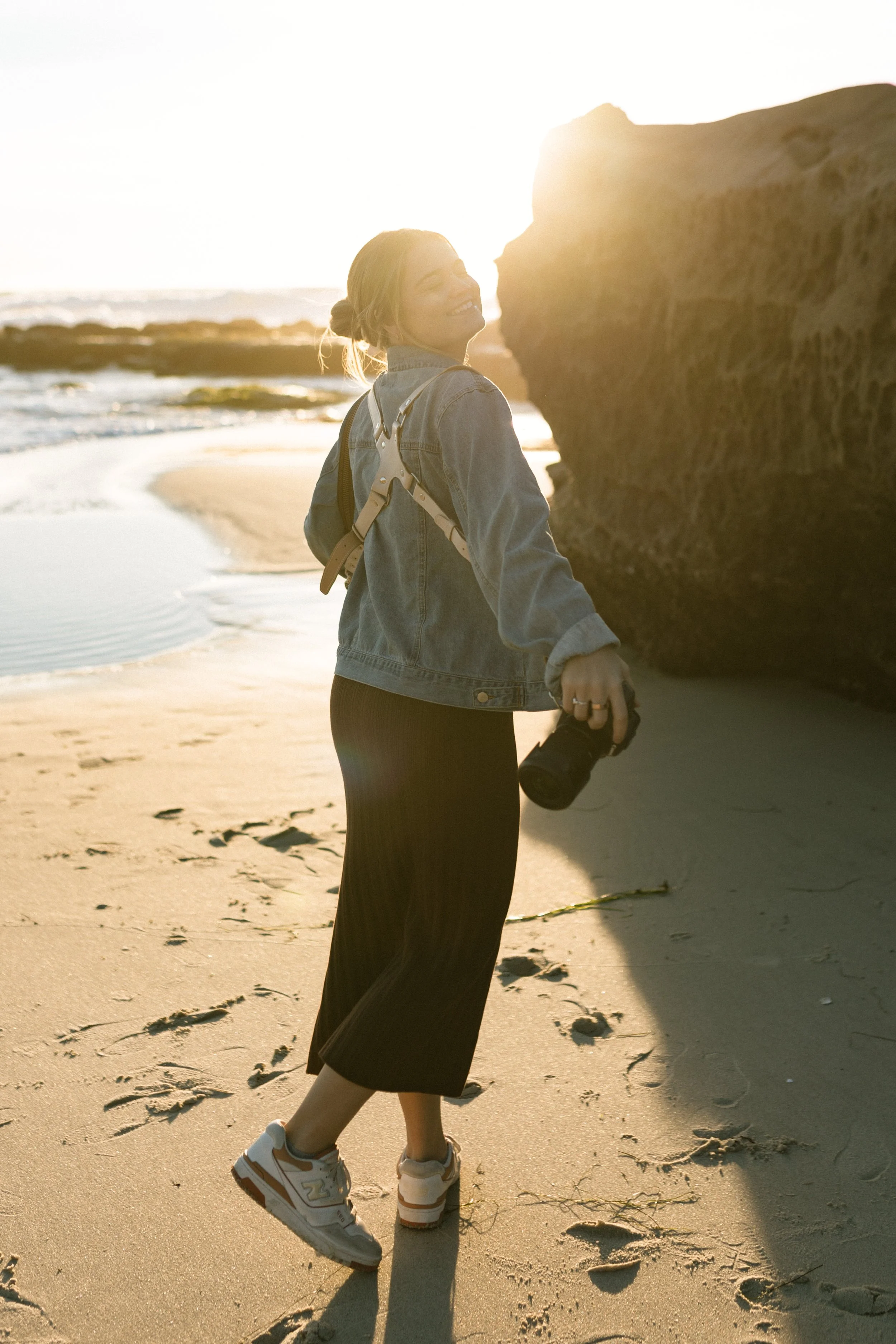 A woman enjoying a sunny day at the beach, holding a camera and smiling.
