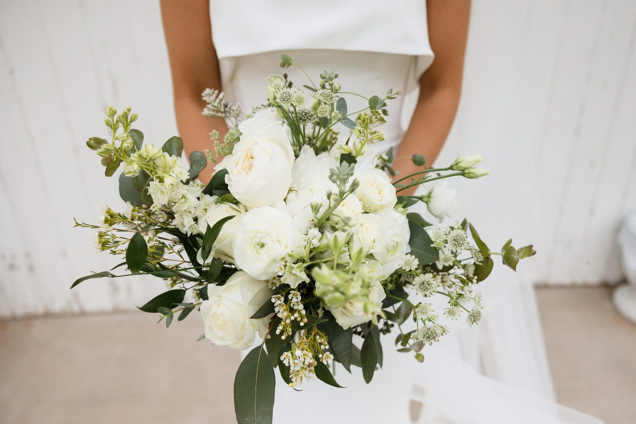 Person holding a bouquet of white and green flowers against a white background.