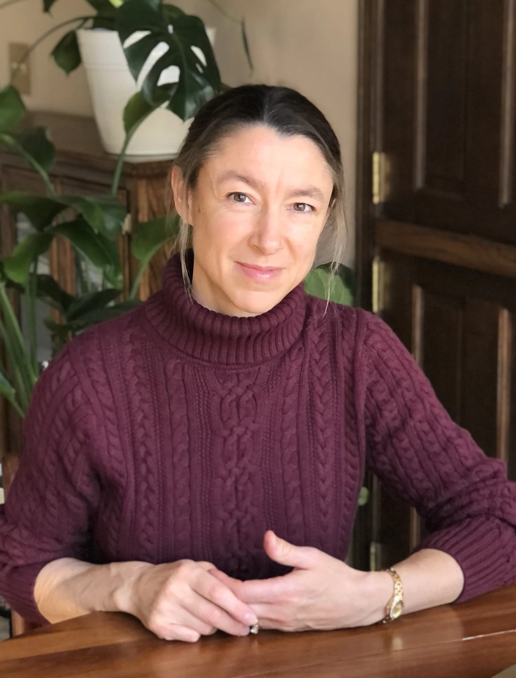 Jennifer Seery, the editor, is sitting at a desk and looking at the camera. She has brown hair and eyes and is wearing a burgundy sweater.
