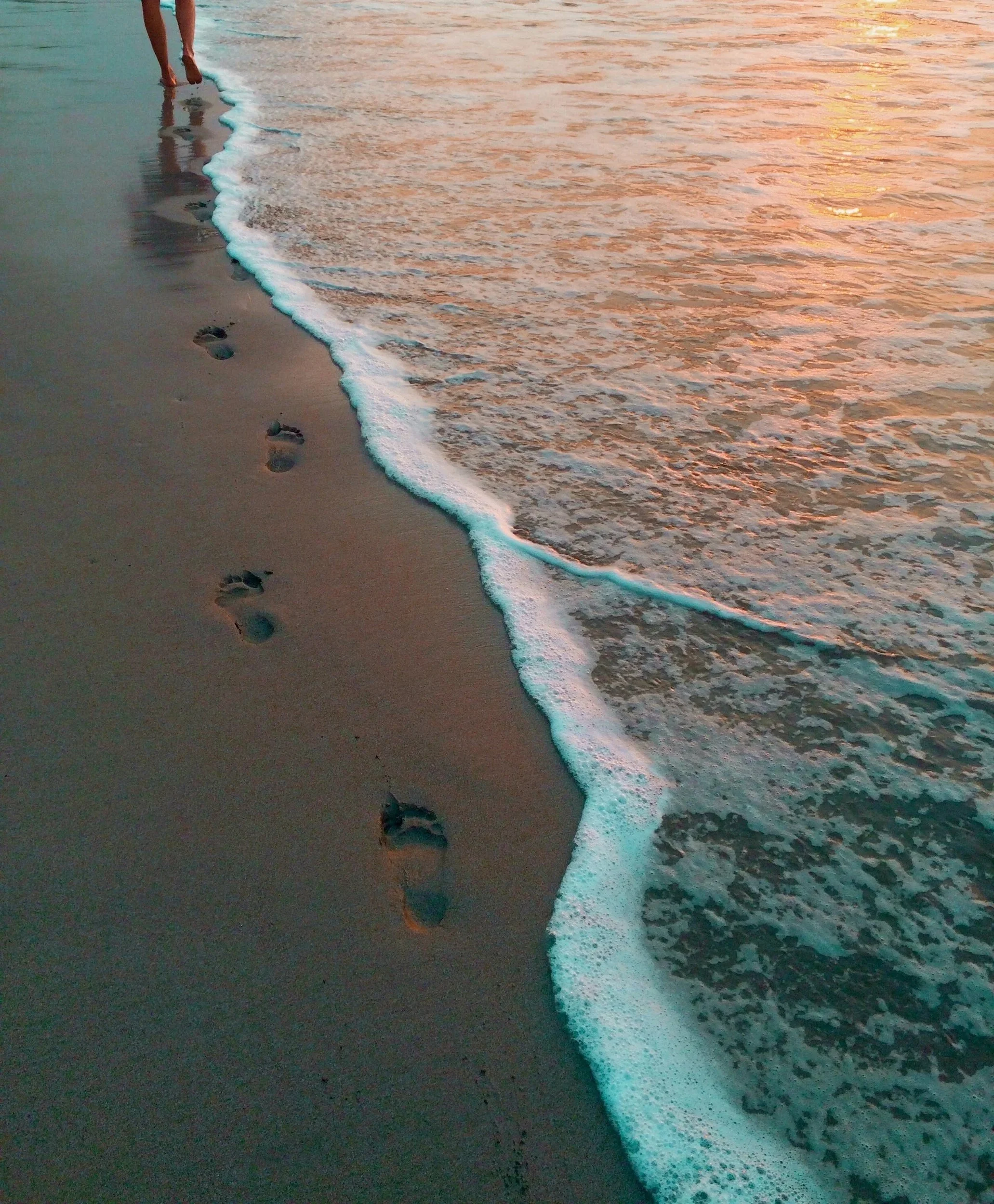 Footprints in wet sand beside the shoreline as gentle waves roll in.