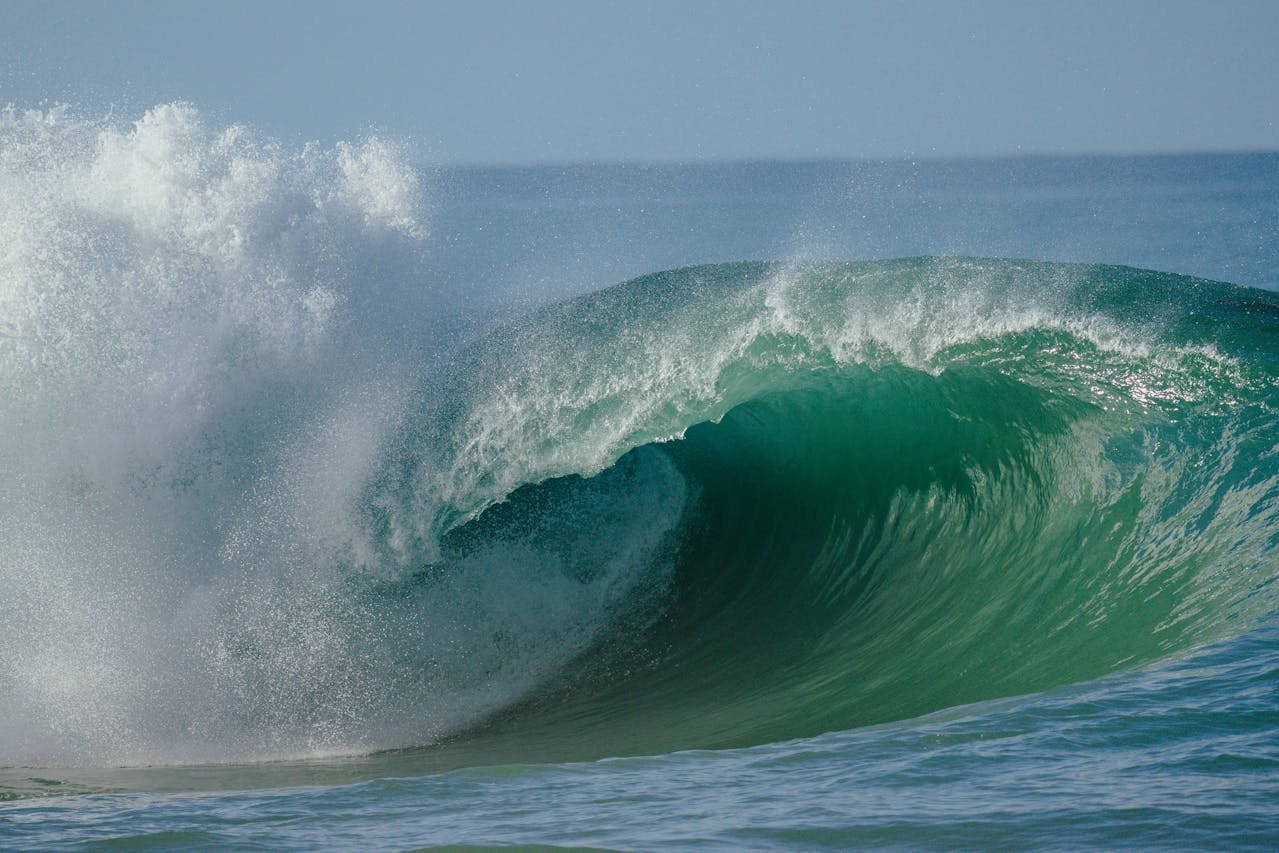 Breaking ocean wave with blue-green water and sea spray under a clear sky.