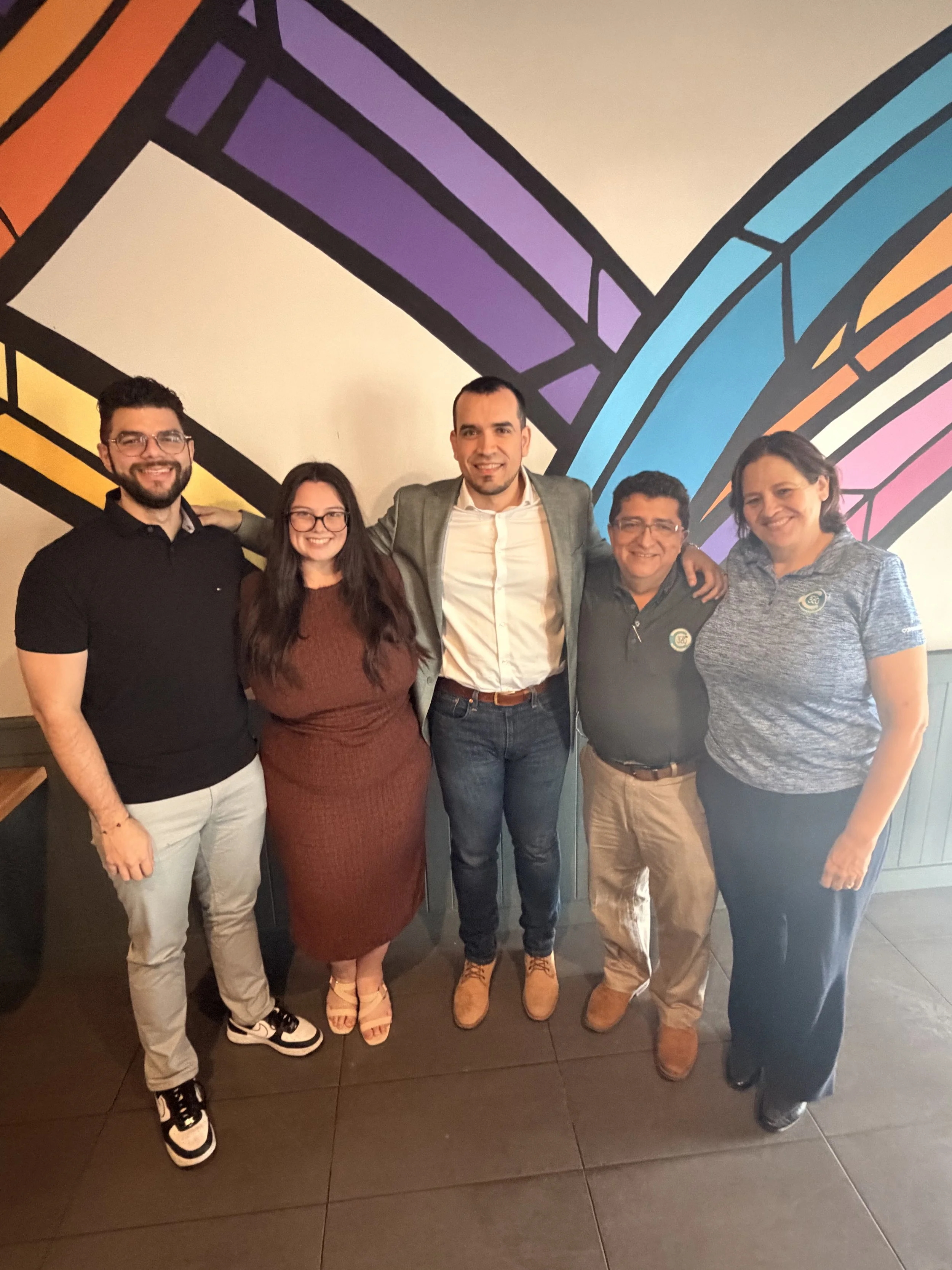Group of five people standing together with a colorful abstract mural in the background