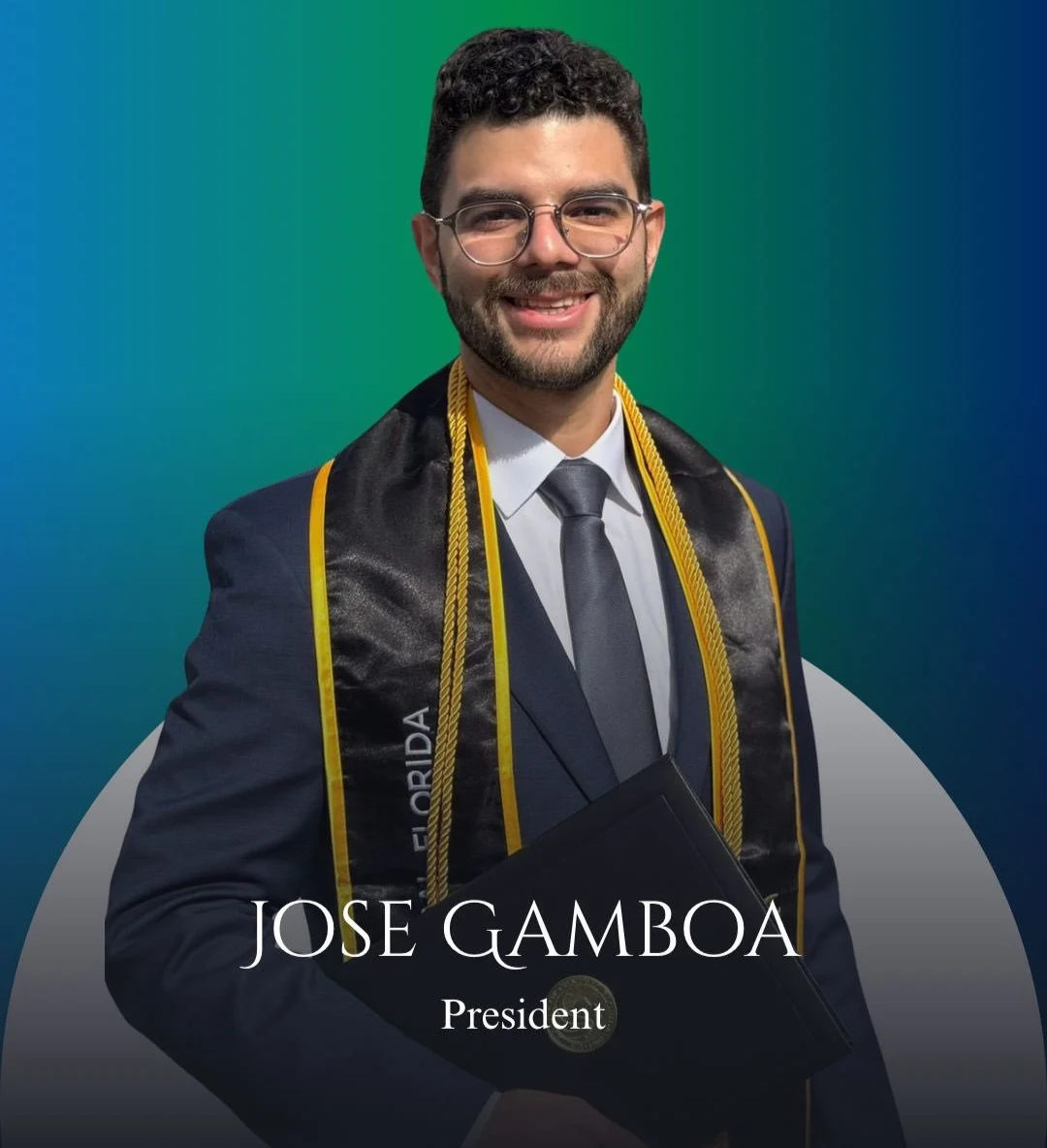 A man in a suit with glasses smiling, wearing a graduation stole and cords, holding a diploma, with a blue and green gradient background.